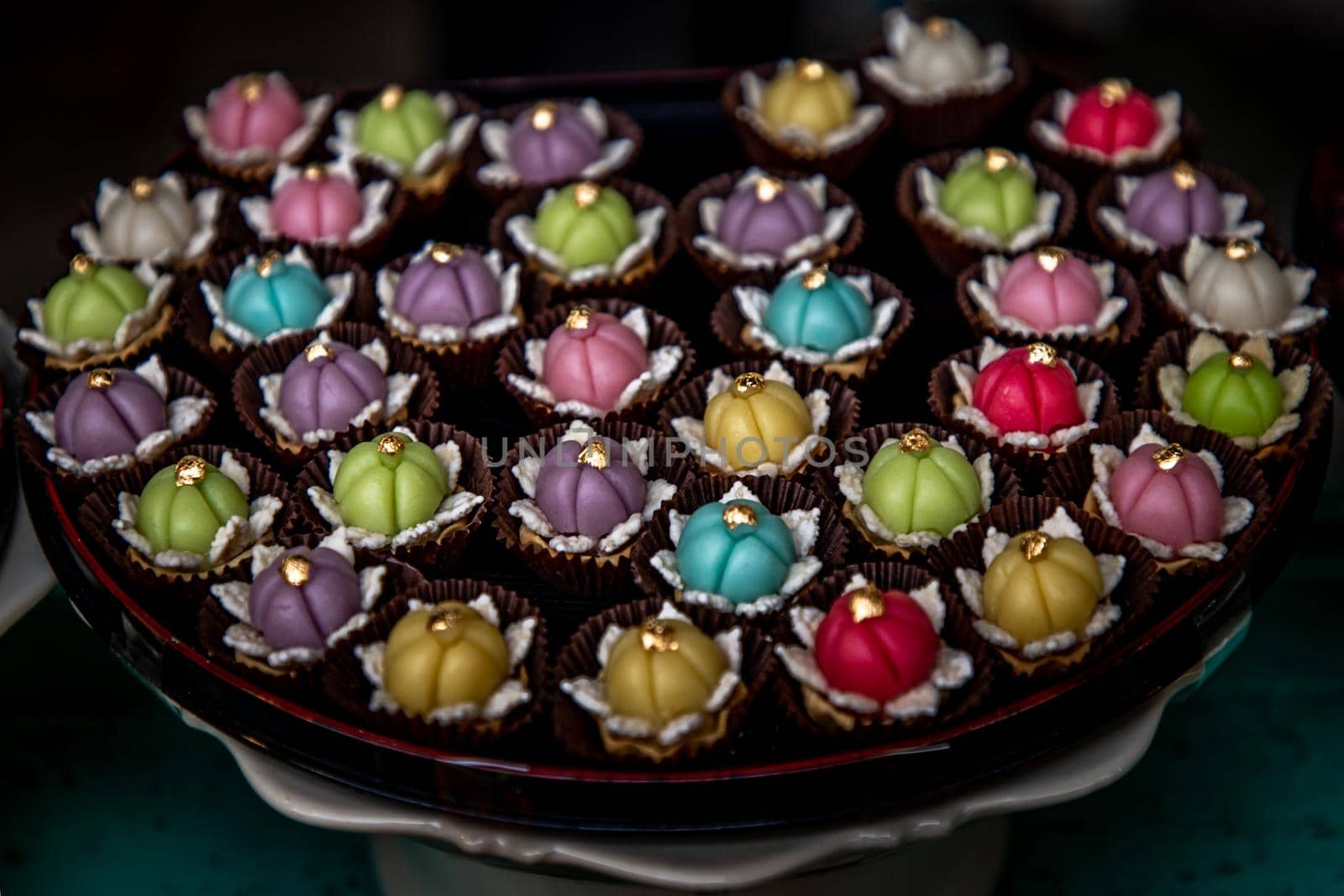 A variety of elegantly beautiful Thai Desserts (Khanom Wan Thai) colorful variations serving in a dark wooden, The bites in gold color and different flower shapes, Thai dessert, Auspicious dessert.