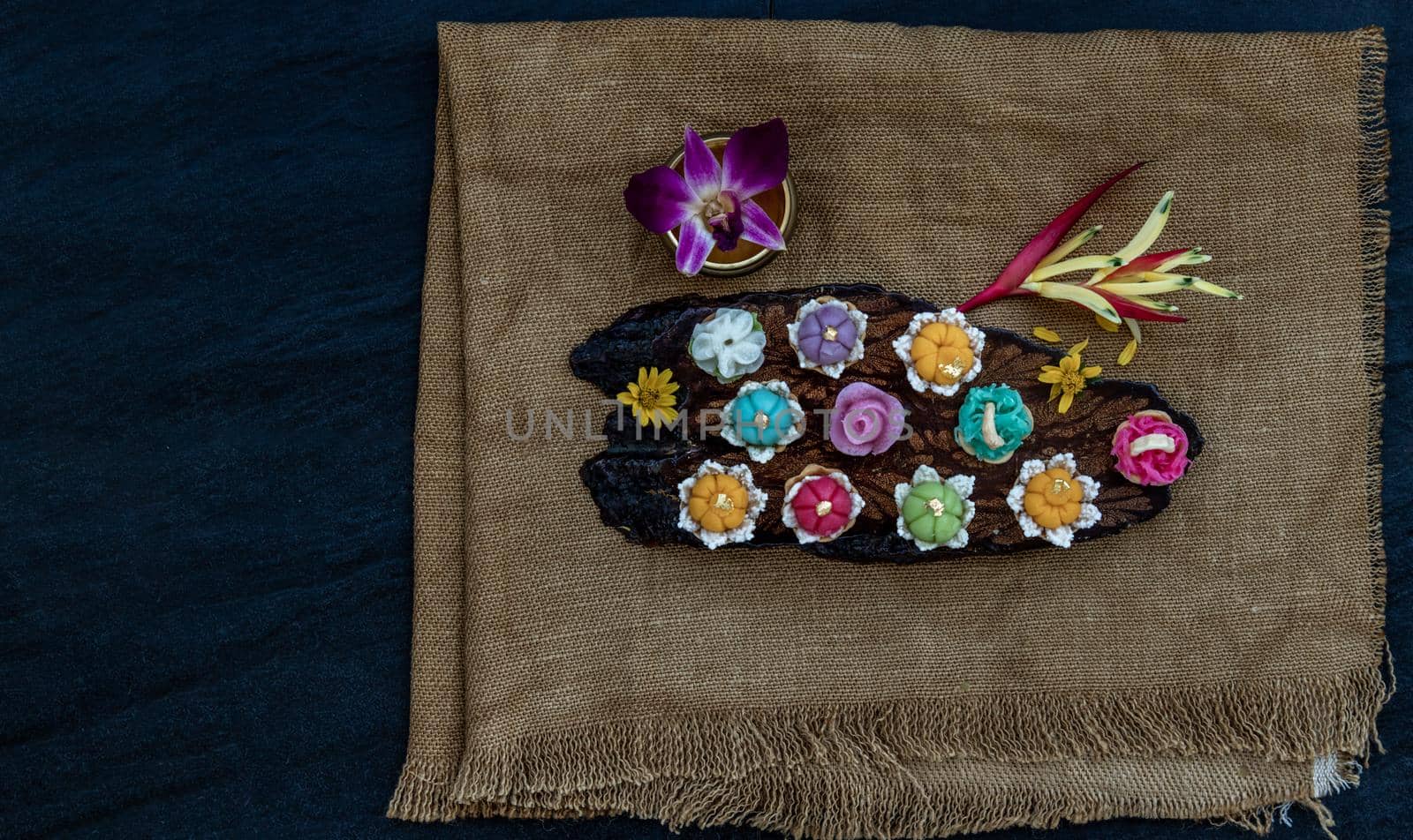 A variety of elegantly beautiful Thai Desserts (Khanom Wan Thai) colorful variations serving in a dark wooden, The bites in gold color and different flower shapes, Thai dessert, Auspicious dessert, Top view.