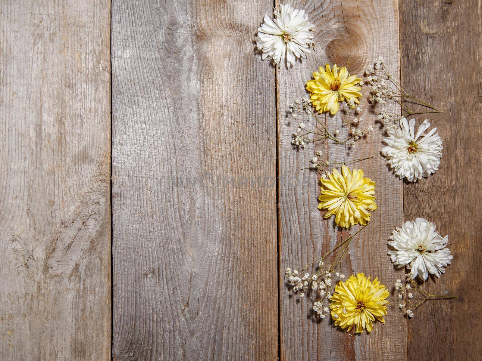 White and yellow flowers lie on wooden surface .