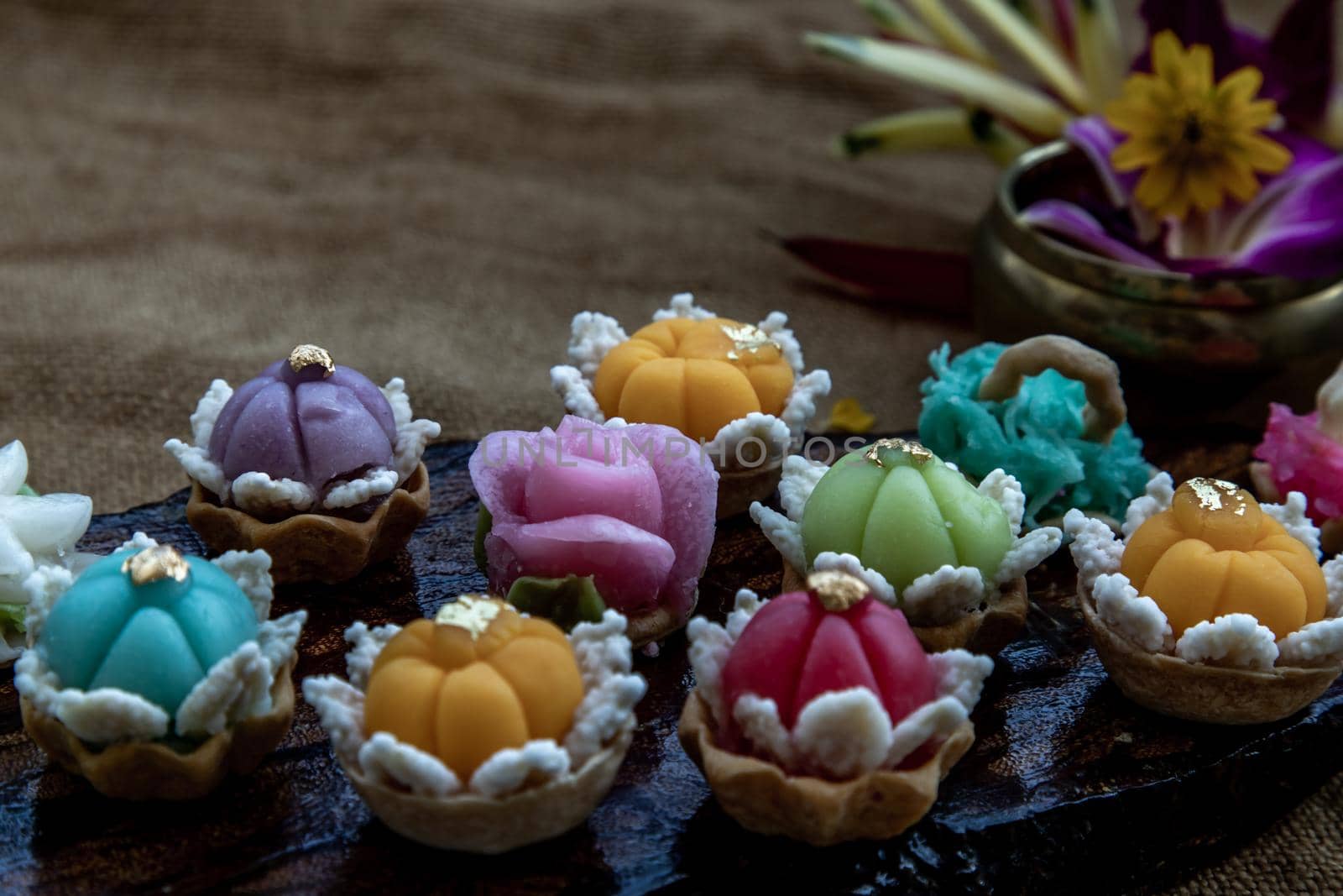A variety of elegantly beautiful Thai Desserts (Khanom Wan Thai) colorful variations serving in a dark wooden, The bites in gold color and different flower shapes, Thai dessert, Auspicious dessert, Oblique view from the top.