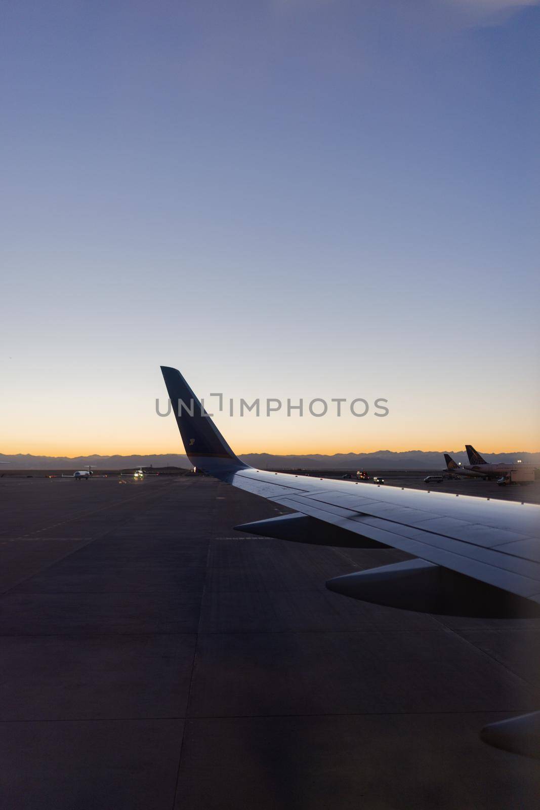 Astonishing view of clear dawn sky above planes parked in airport. Beautiful view of bright sunrise skyline from behind an airplane wing. Transportation and landscapes