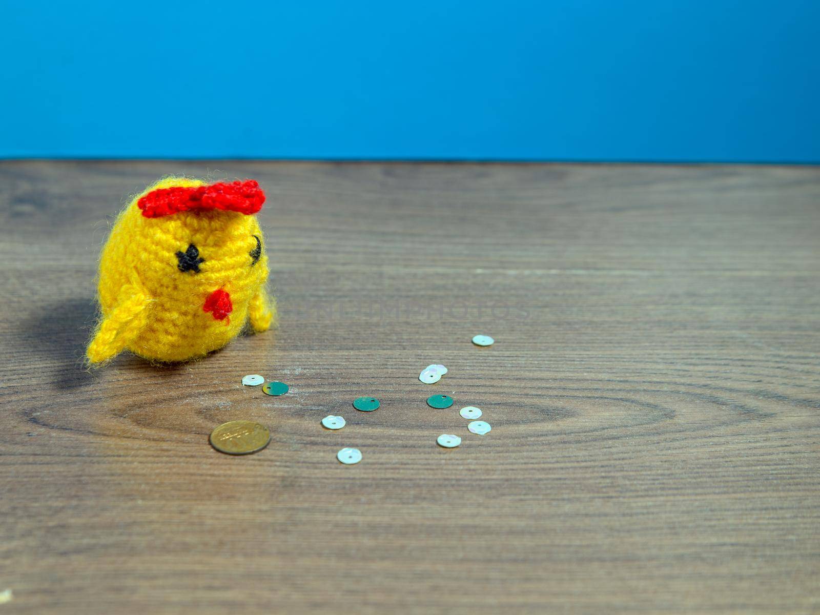 Toy yellow chicken and coin next to tinsel on brown table.