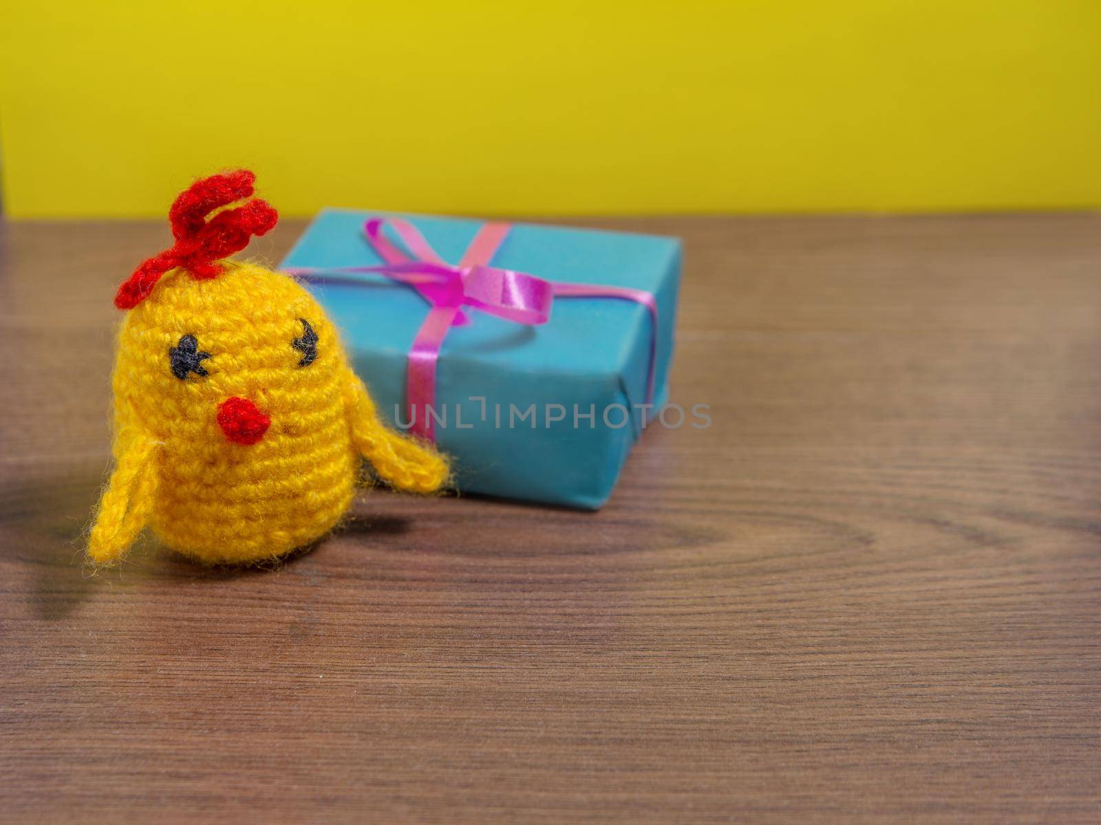 Toy yellow chicken next to gift in blue wrapper on brown table.