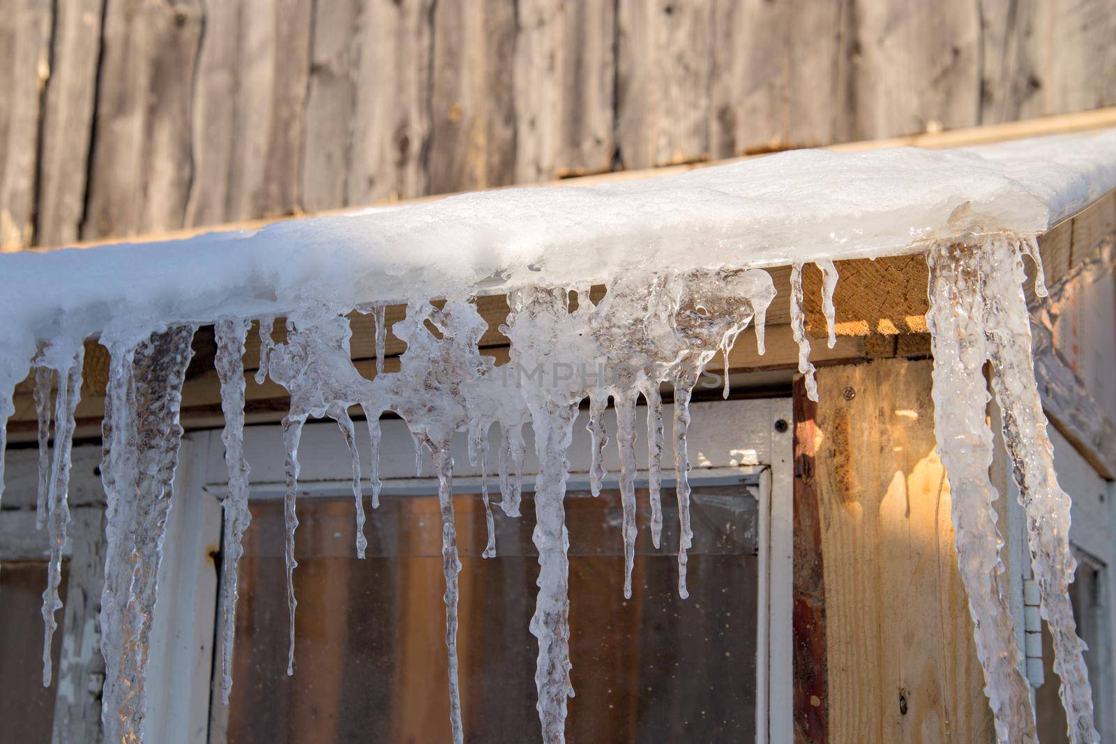 Spring ice icicles on roof of greenhouse. Patterns scattered by sun and frost. Selective focus