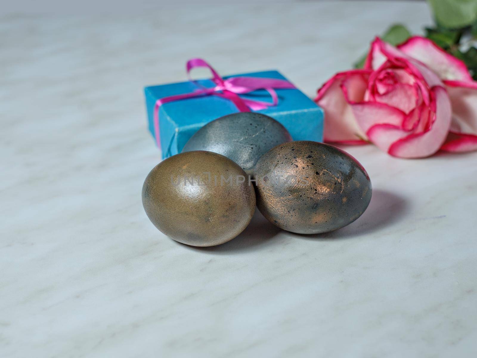 Painted for Easter egg, box with gift and bouquet of roses lie on gray table. Selective focus