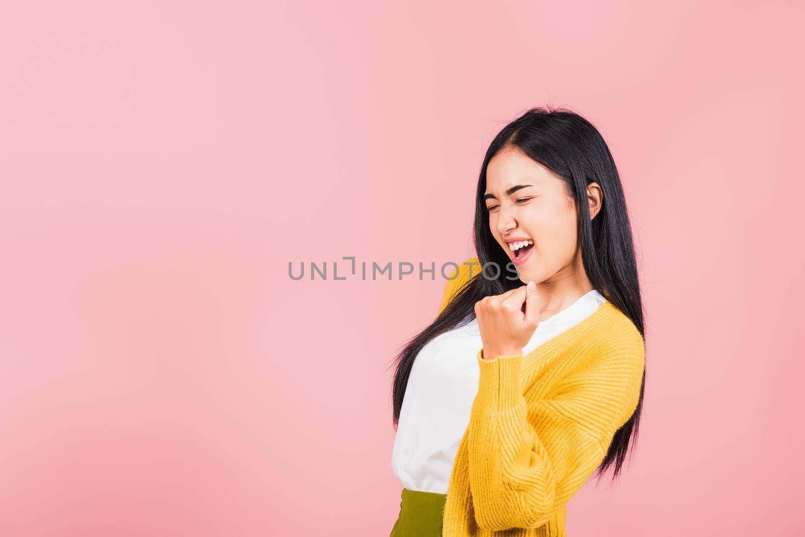 Happy Asian portrait beautiful cute young woman stand makes raised fists up celebrating her winning success gesture, studio shot isolated pink background, Thai female excited say yes! with copy space