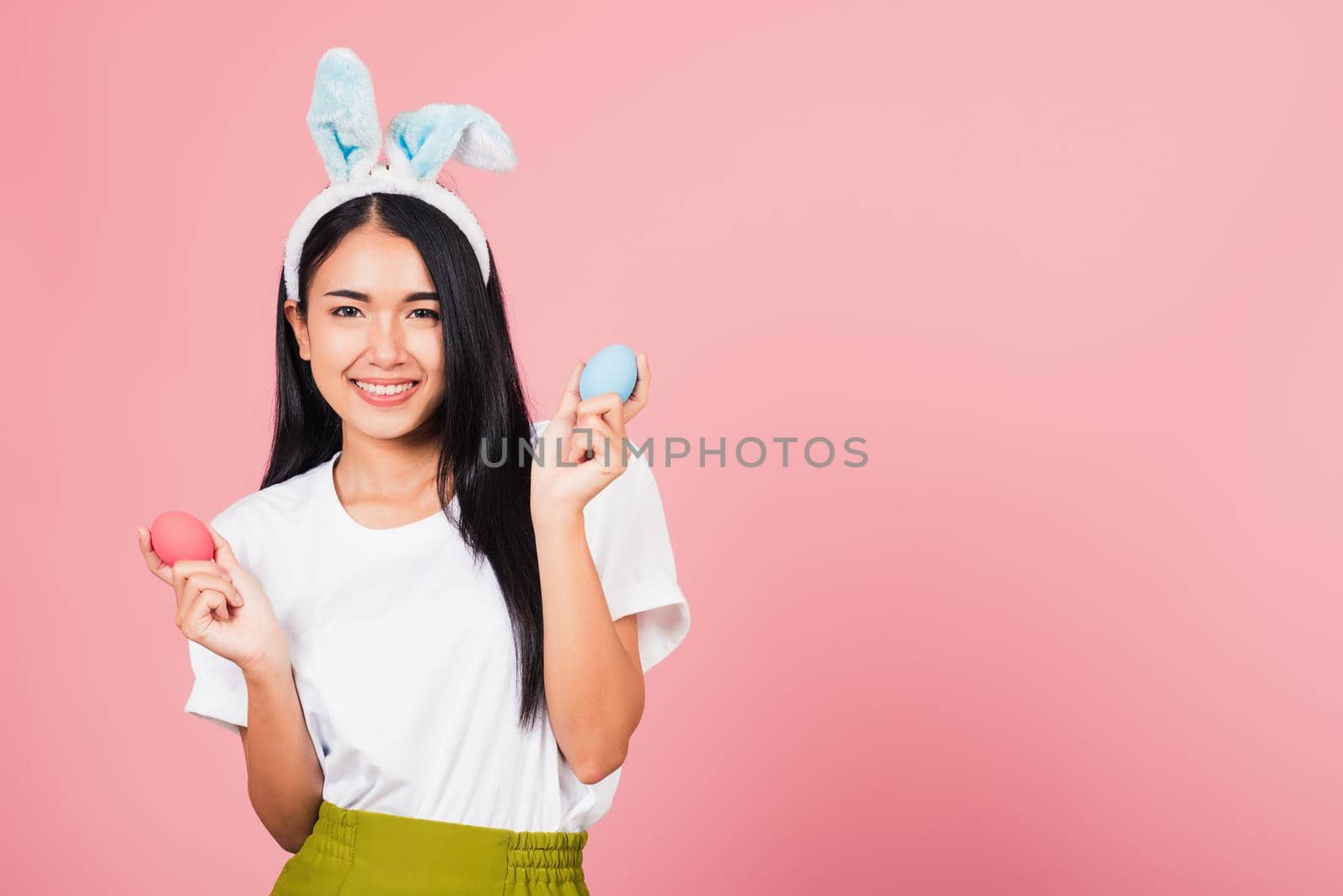 Happy Easter concept. Beautiful young woman smiling wearing rabbit ears holding colorful Easter eggs gift on hands, Portrait female looking at camera, studio shot isolated on pink background