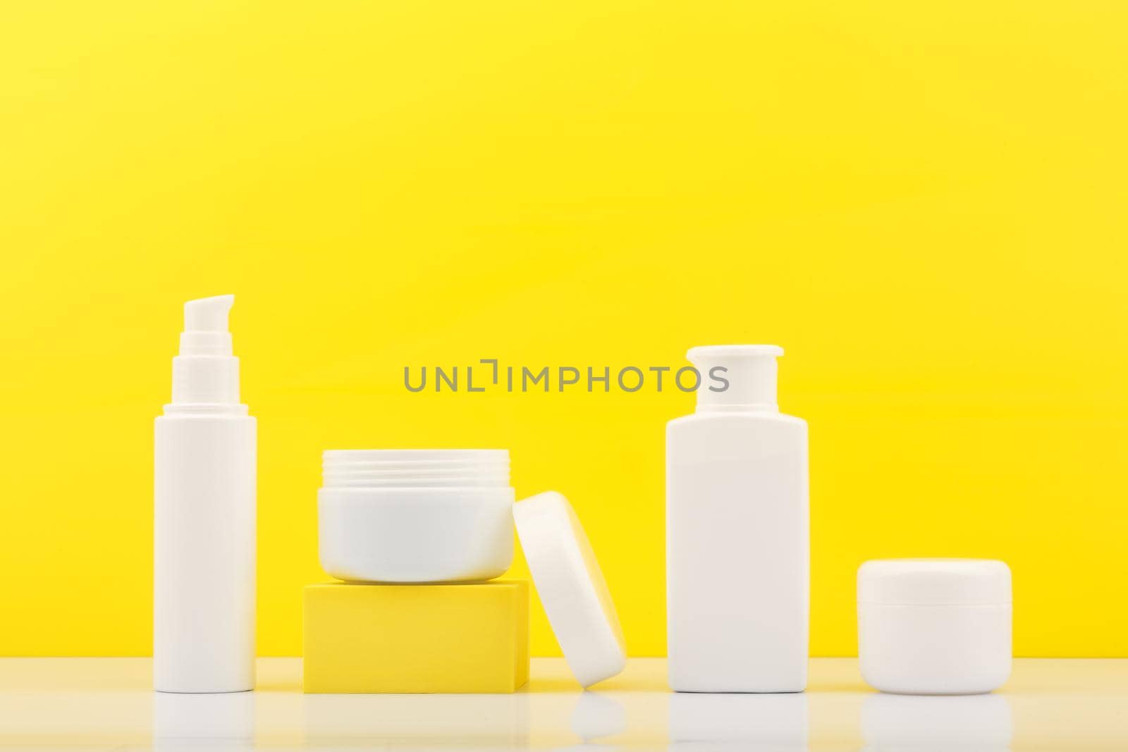Set of cosmetic bottles with products for skin care against bright yellow background by Senorina_Irina