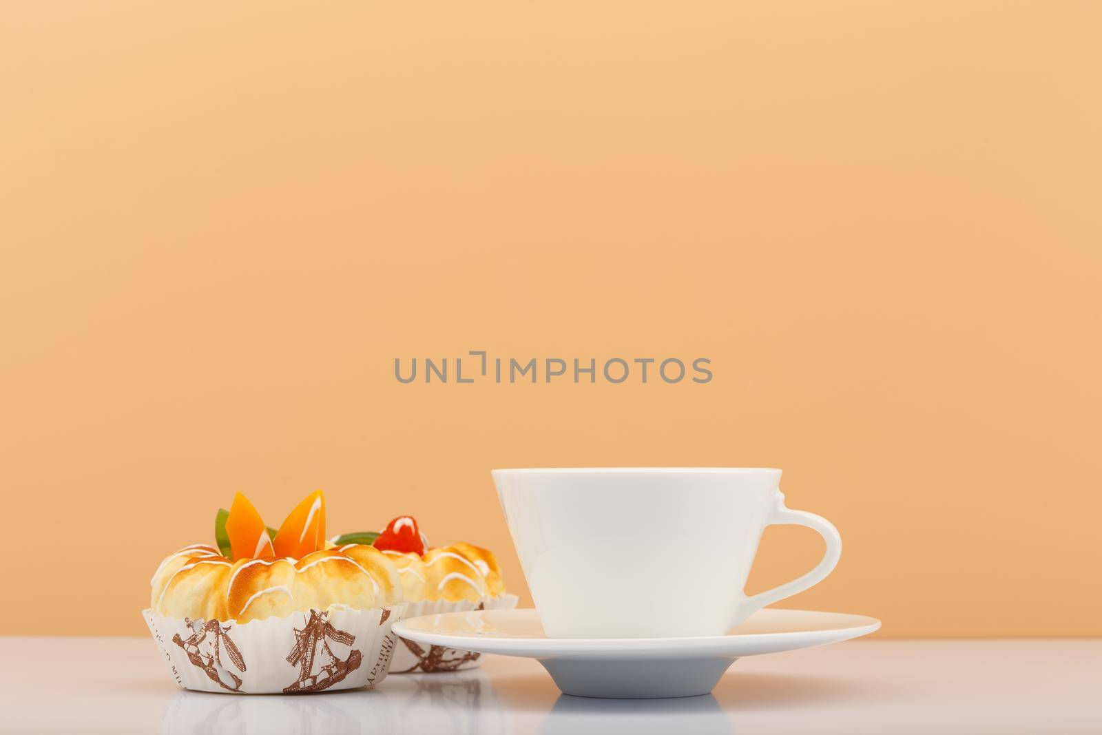 White ceramic tea or coffee cup with sweets next to it against beige background with copy space. High quality photo