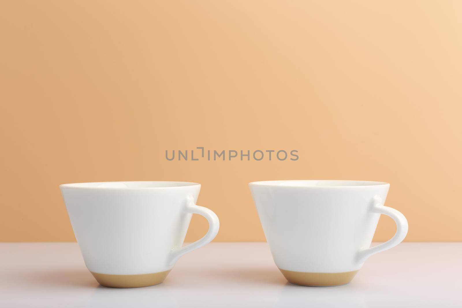 Close up of two white ceramic coffee cups on white table against beige background. High quality photo