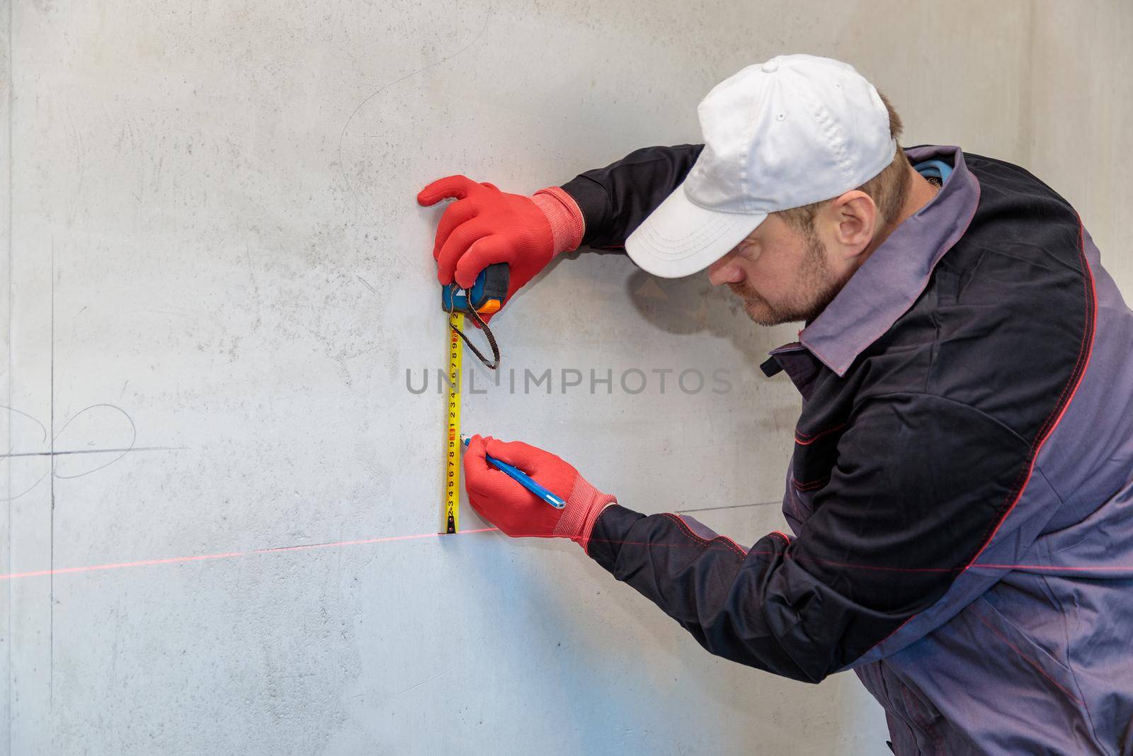 A man, an electrician marks out with a pencil, tape measure and a linear level for drilling holes for sockets