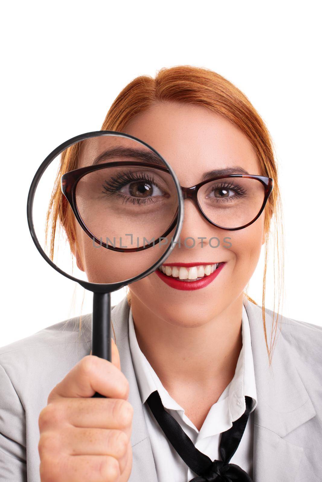 Close up of a beautiful young businesswoman smiling and looking through magnifying glass, isolated on white background. Analysis, scrutiny concept.