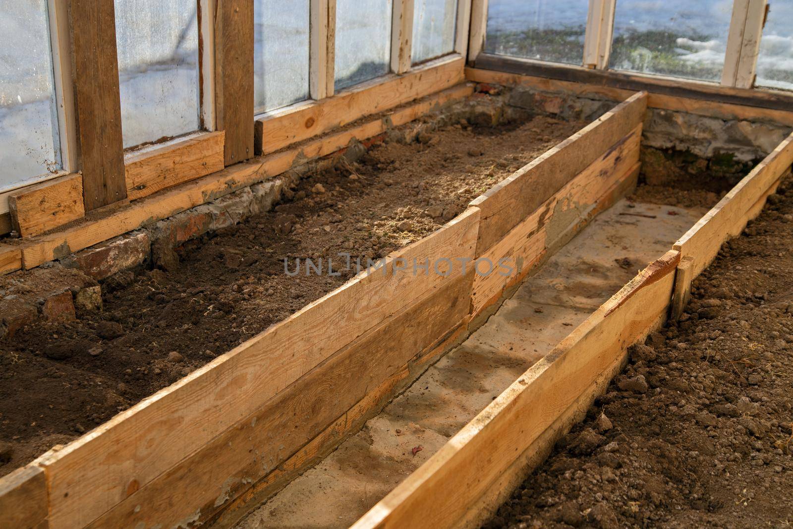 Separated by boards, beds with wet ground in makeshift greenhouse.