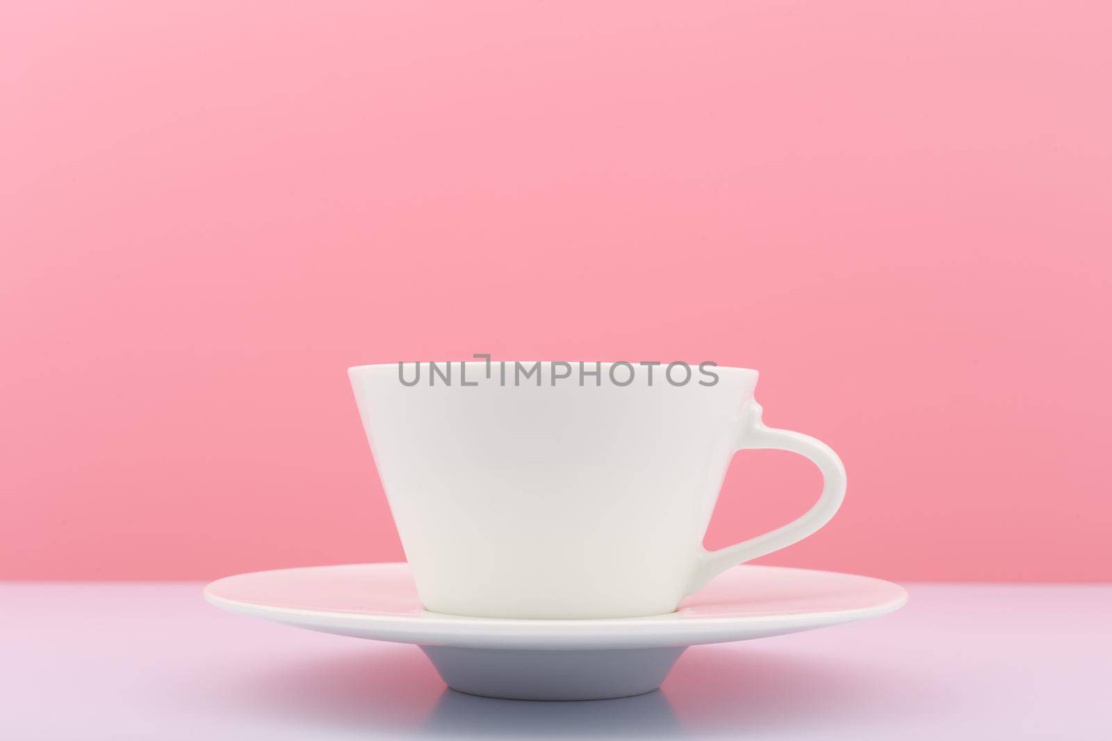 Close up of white ceramic coffee cup with saucer on white table against bright pink background by Senorina_Irina