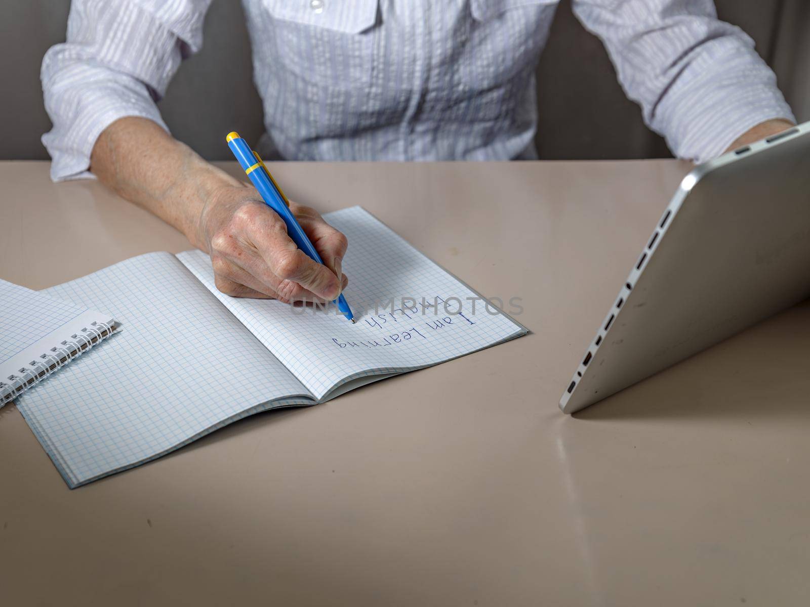 Notebook, hand with pen, tablet on light table. Online English language training by Sestra