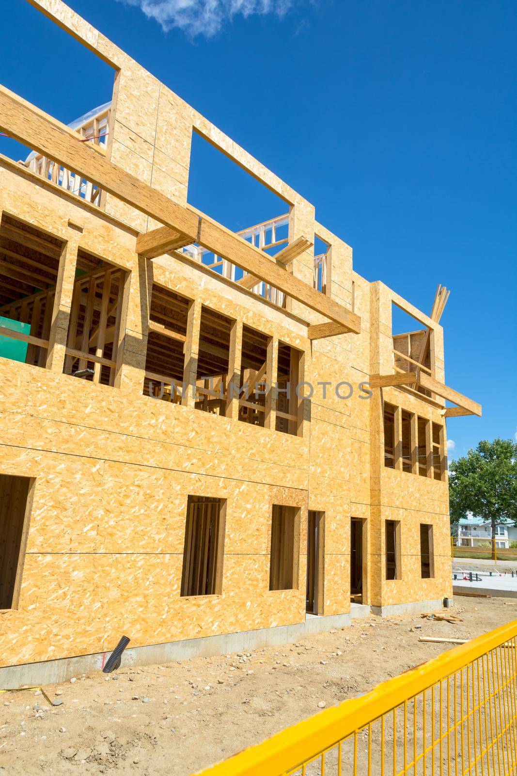 New residential building under construction with metal fence in front. Low rise wooden framework of the building on concrete base
