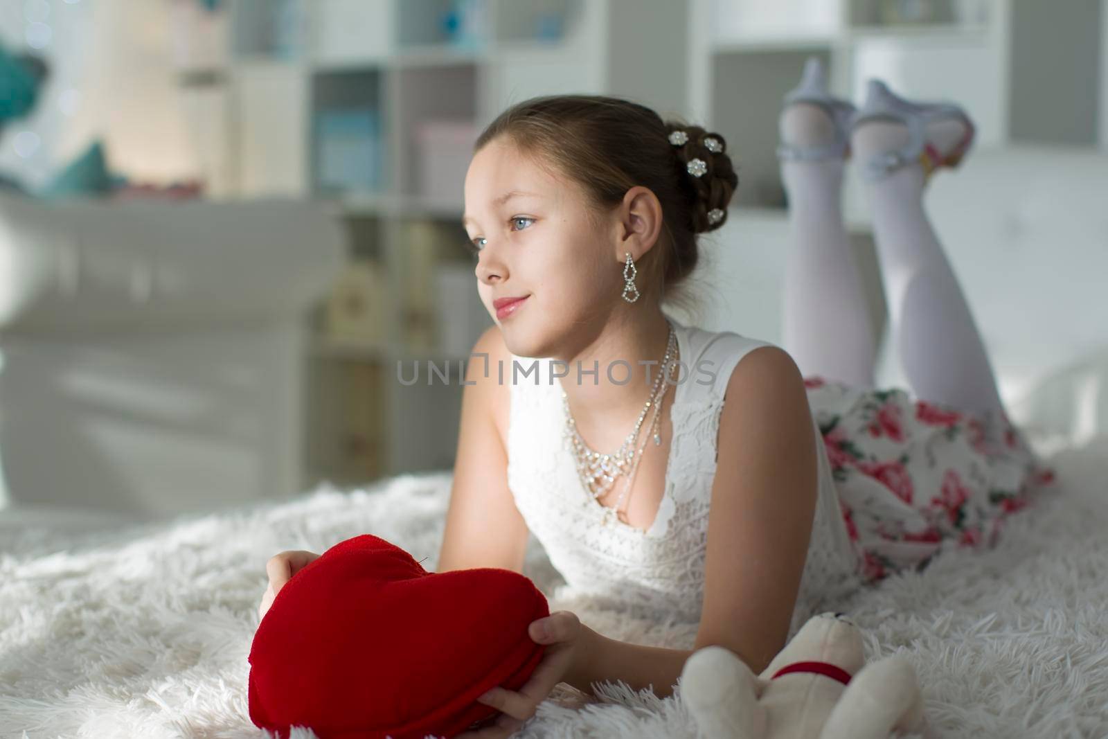 Very beautiful teen girl lying on a bed with a red heart pillow.Young lady