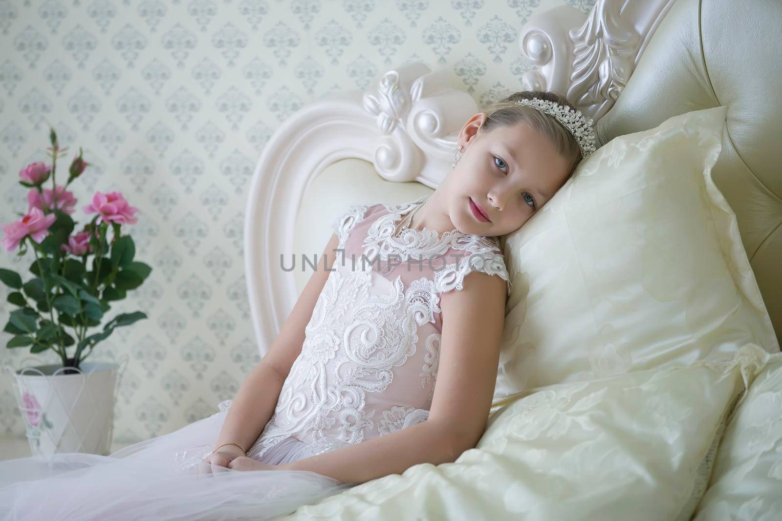 Cute tender girl teenager lies on the bed. Princess in a white dress with a crown. by Sviatlana