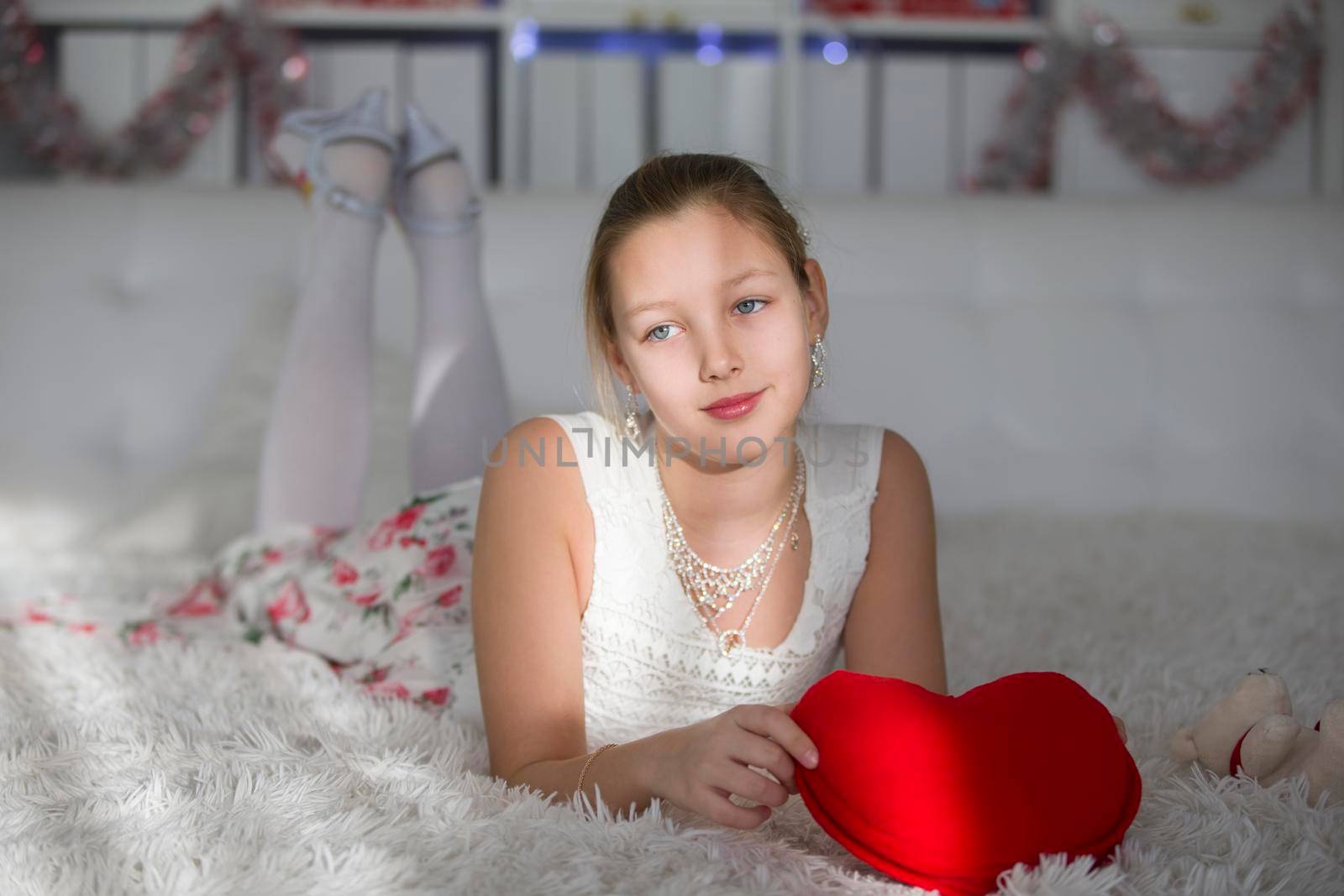 Very beautiful teen girl lying on a bed with a red heart pillow.Cute tender girl teenager dreams. Young lady