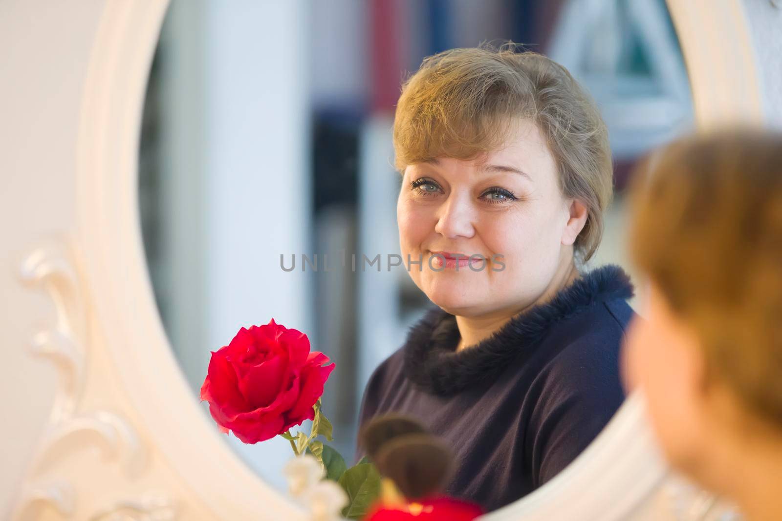 An ordinary full lonely woman with a rose looks in the mirror. Middle age crisis by Sviatlana