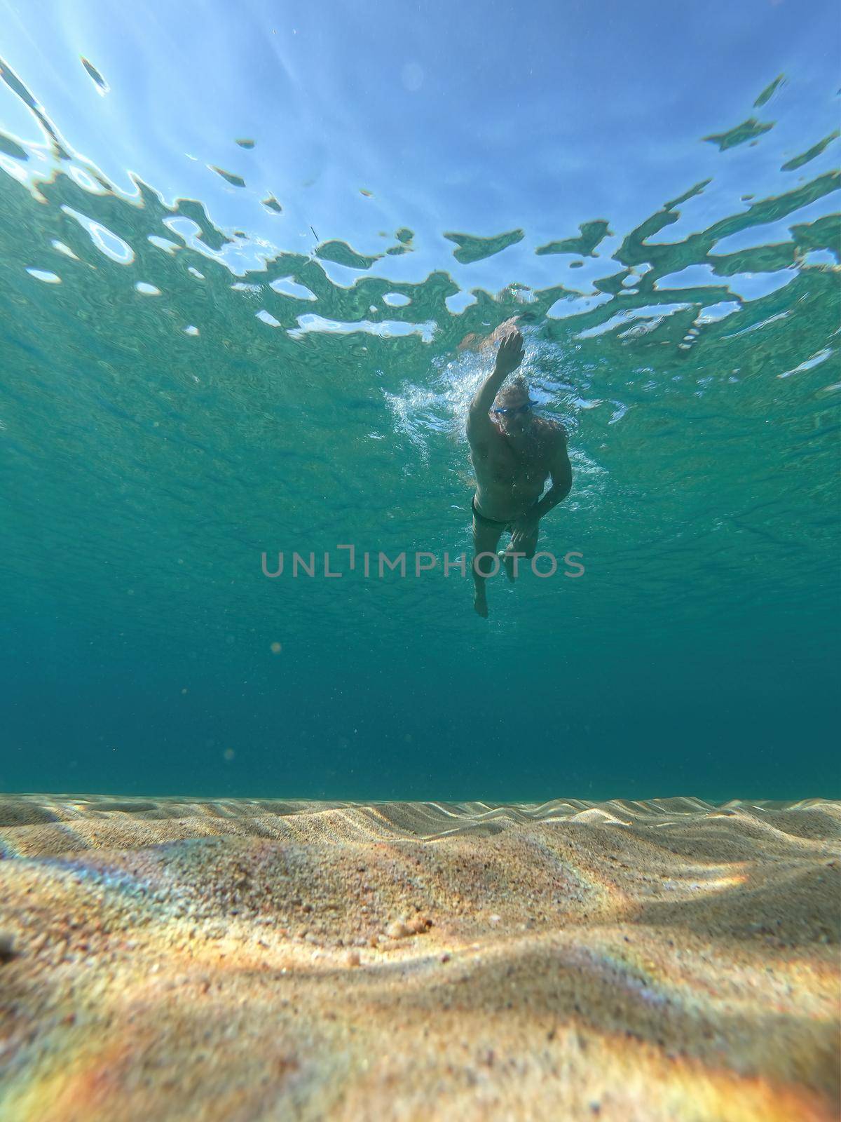 Sporty man swimming in a clear sea water in Spanish Costa Brava in summer by Digoarpi