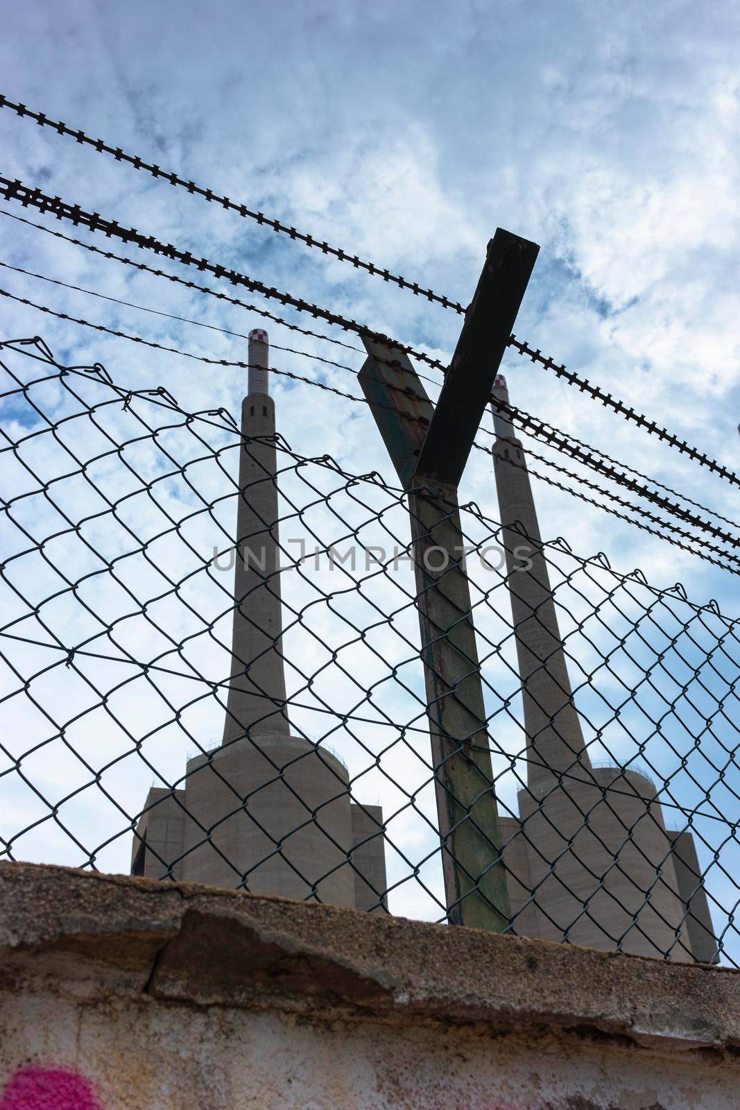 Old disused thermal power plant for the production of electricity in Barcelona behind a metal fence by loopneo