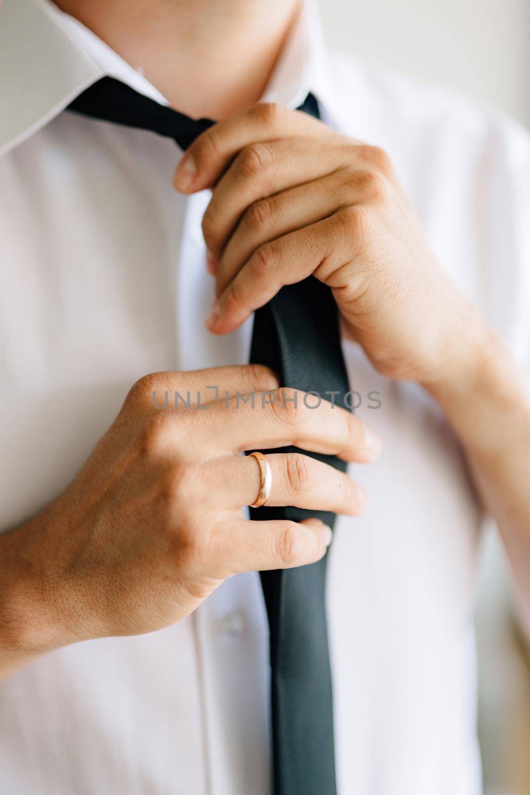 A man puts on and ties a tie while preparing for a wedding ceremony, close-up . High quality photo