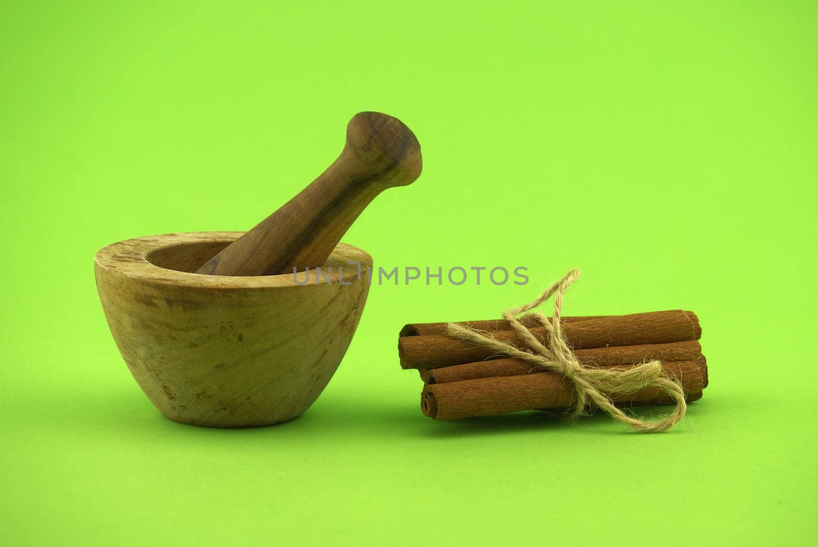 Cinnamon sticks bundle tied with jute string and wooden mortar with pestle on green background and free copy space for text