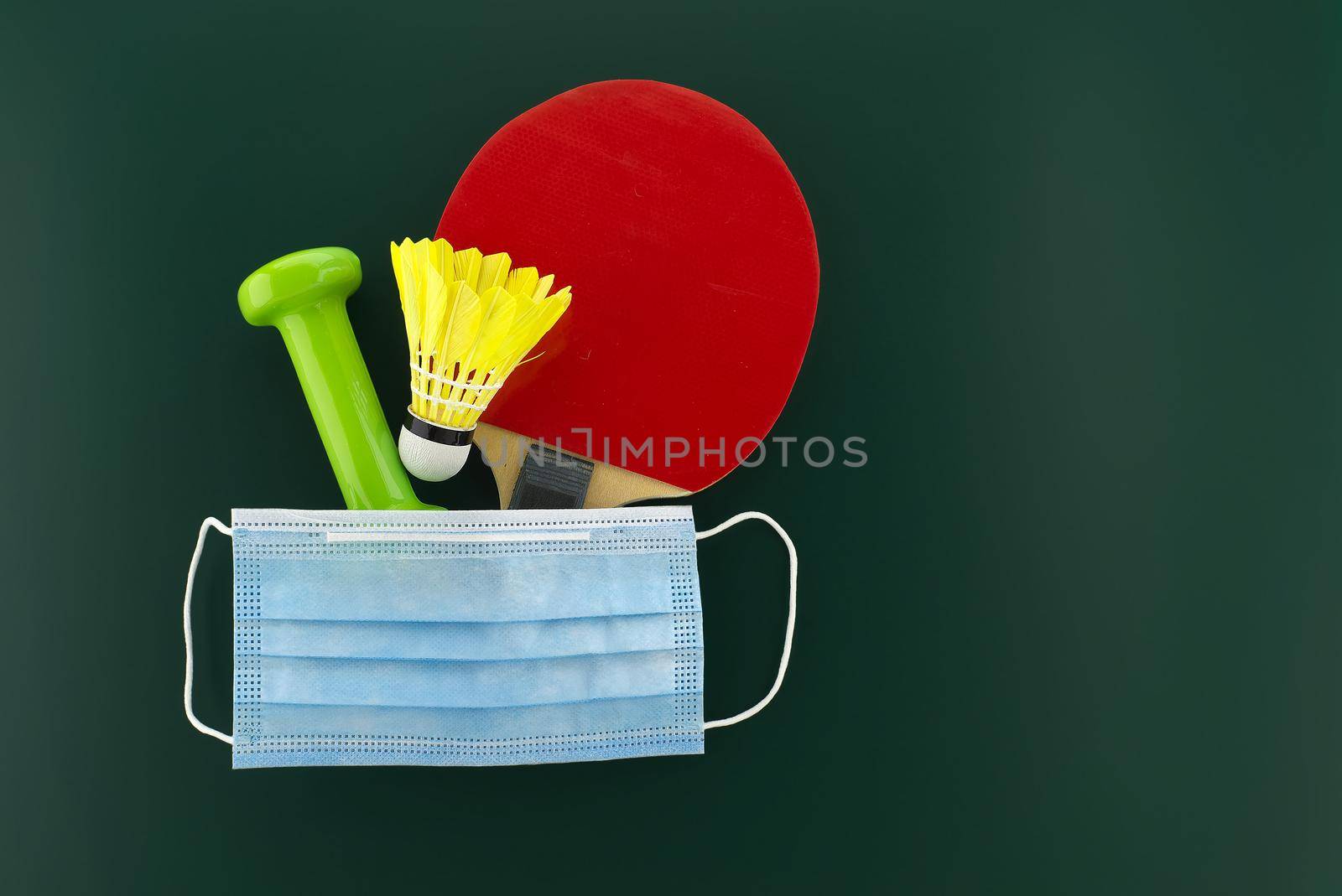 Dumbbells, shuttlecock, table tennis racket cover with a medical face mask. Sports during the quarantine period concept with free copy space