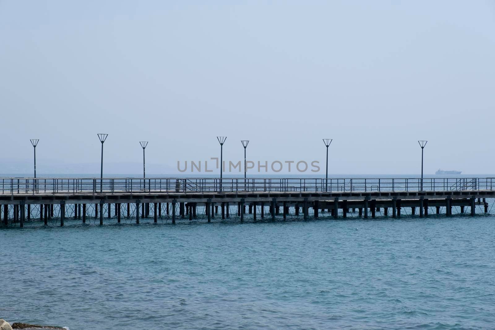 Shot of the open sea on a clear sunny day. Blue sky, pier, ships in the distance and boundless horizon.