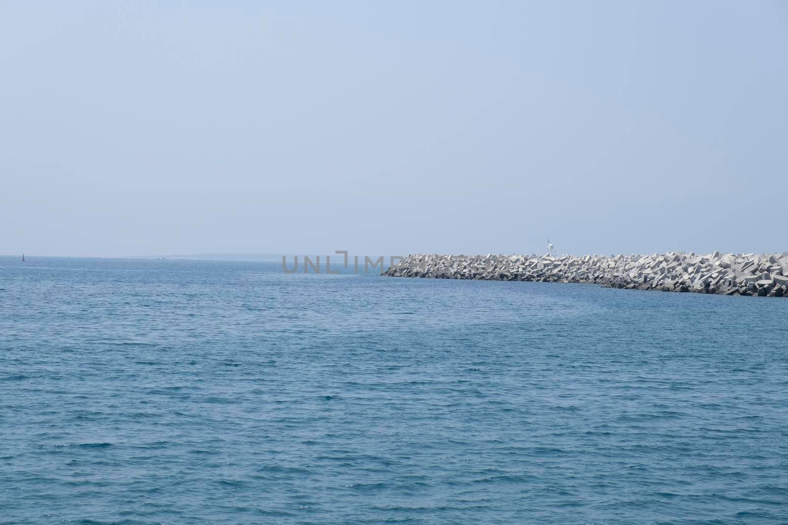 Aerial shot of the open sea on a cloudy day. Blue sky, pier, ships in the distance and boundless horizon.