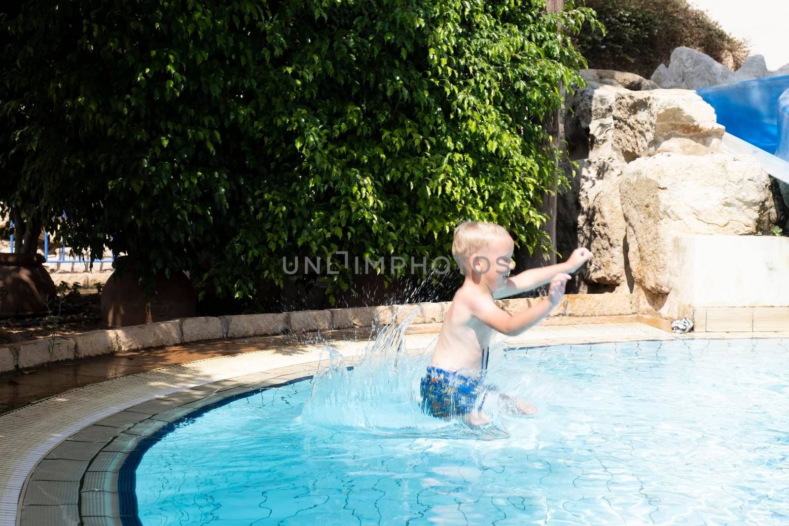 A happy smiling child jumps and dives under the water in the pool on a clear day. by designprojects