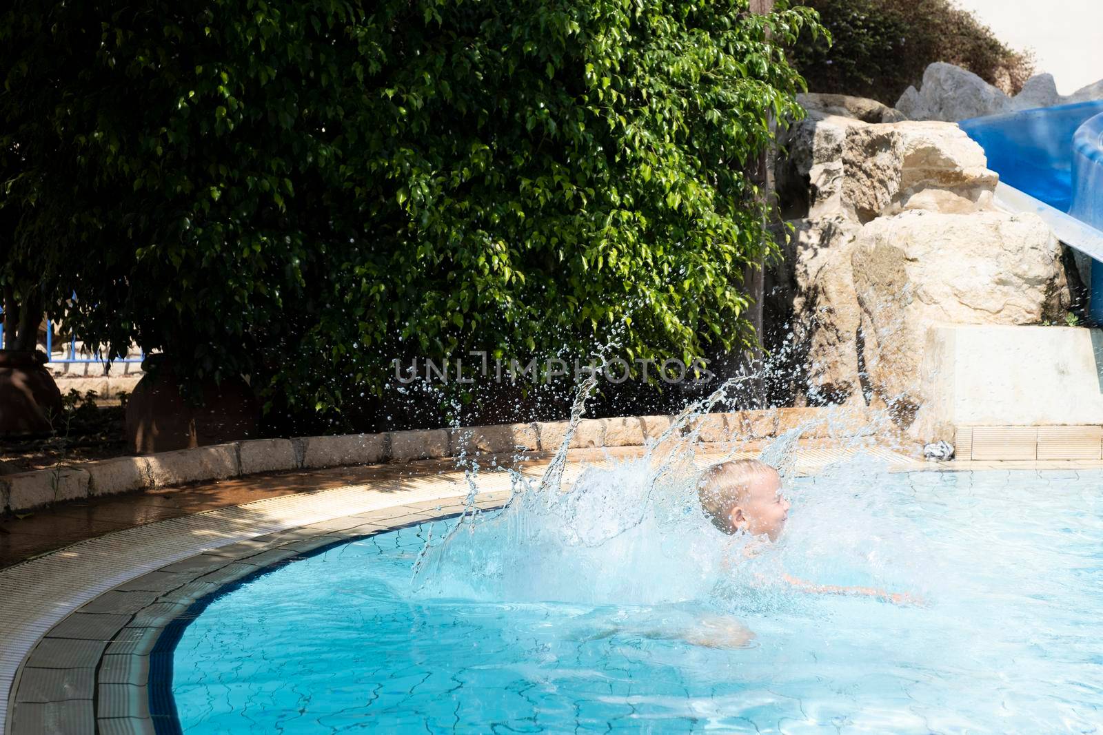 A happy smiling child jumps and dives under the water in the pool on a clear day. by designprojects