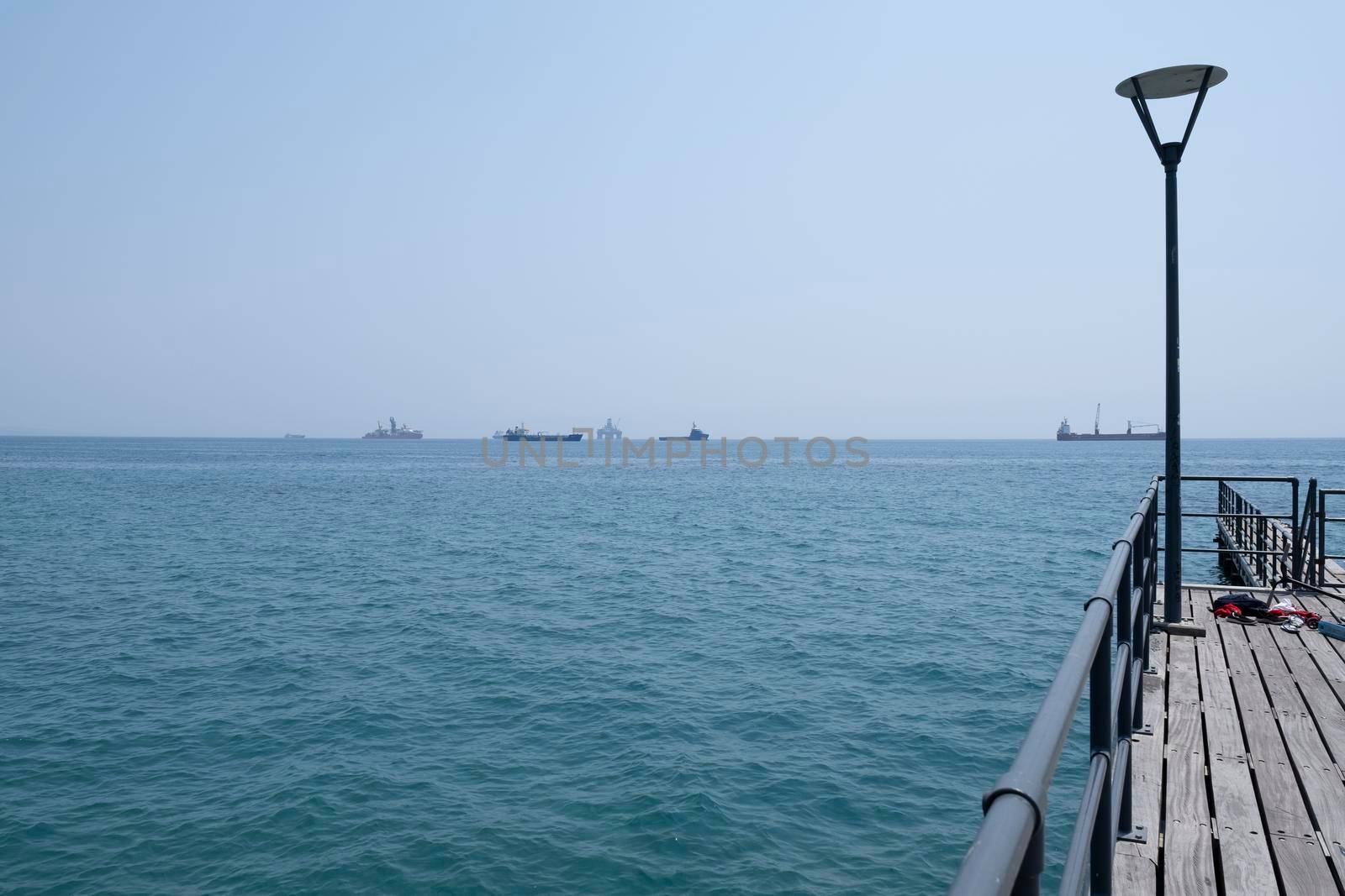 Shot of the open sea on a clear day. Blue sky, pier, ships in the distance and boundless horizon. by designprojects