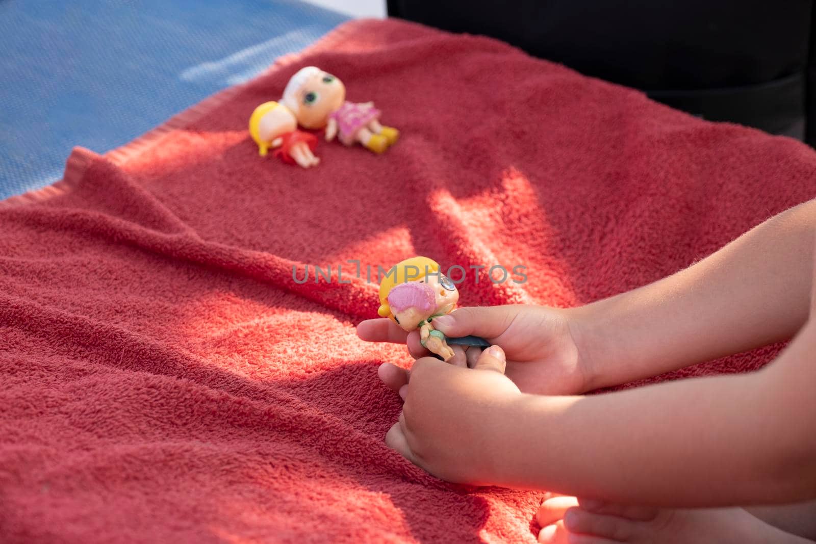 Cute girl playing with her dolls on a sunbed on a sandy beach on a sunny day.