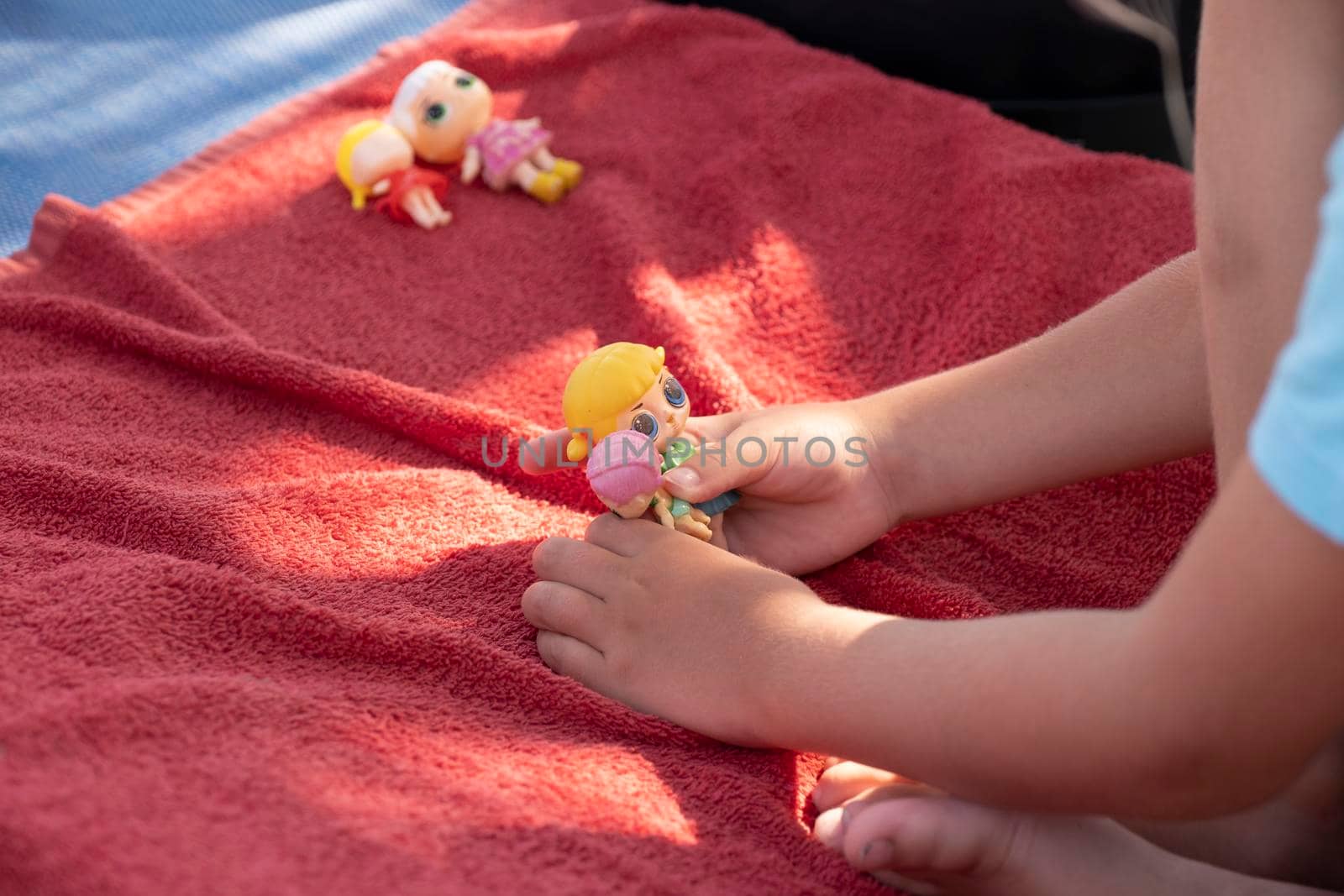 Cute girl playing with her dolls on a sunbed on a sandy beach on a sunny day.