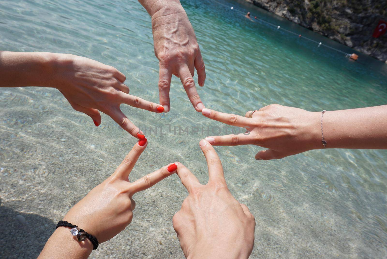 Five hands building a star shape by finger connection in front of sea. Happy Friends or family on vacation. Beach holidays concept.