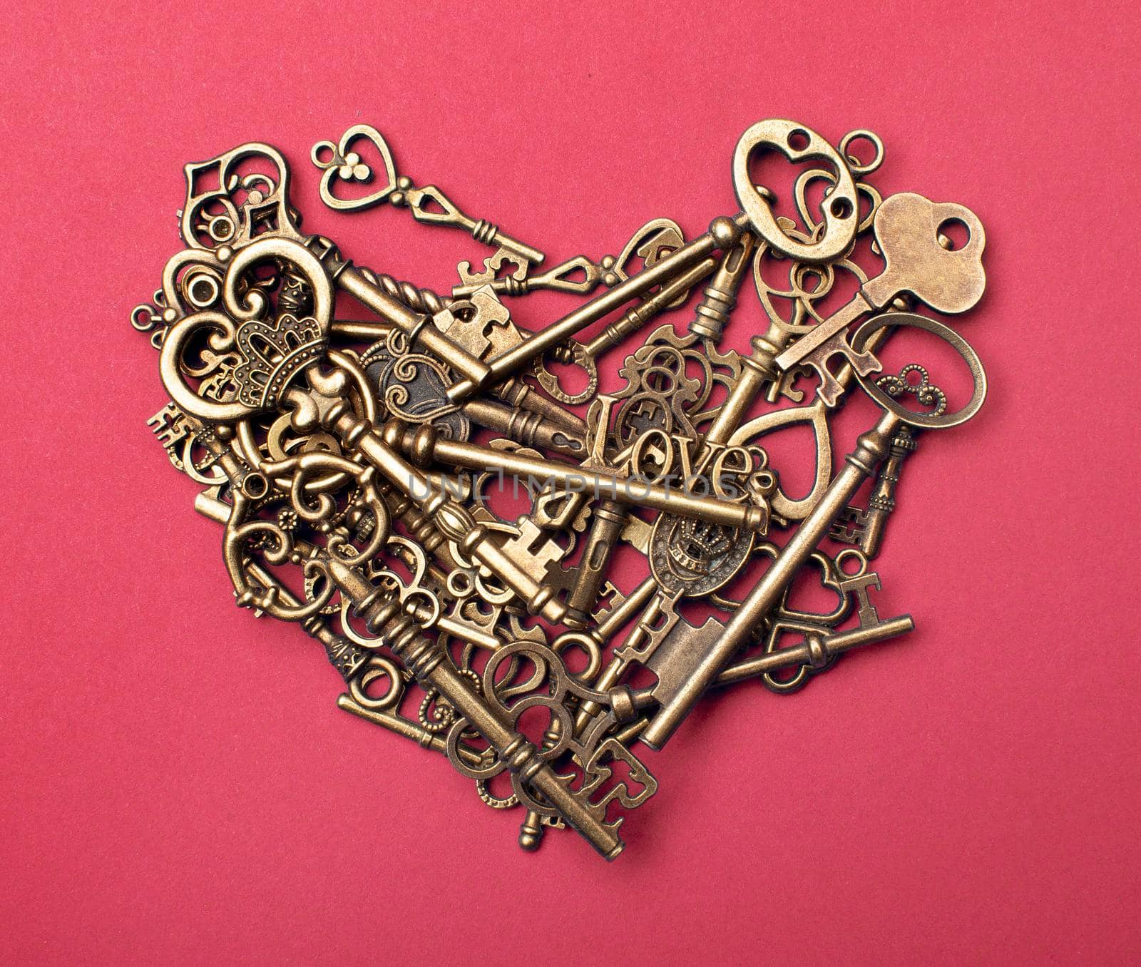 Old, vintage keys in the shape of a heart isolated on pink color bacground