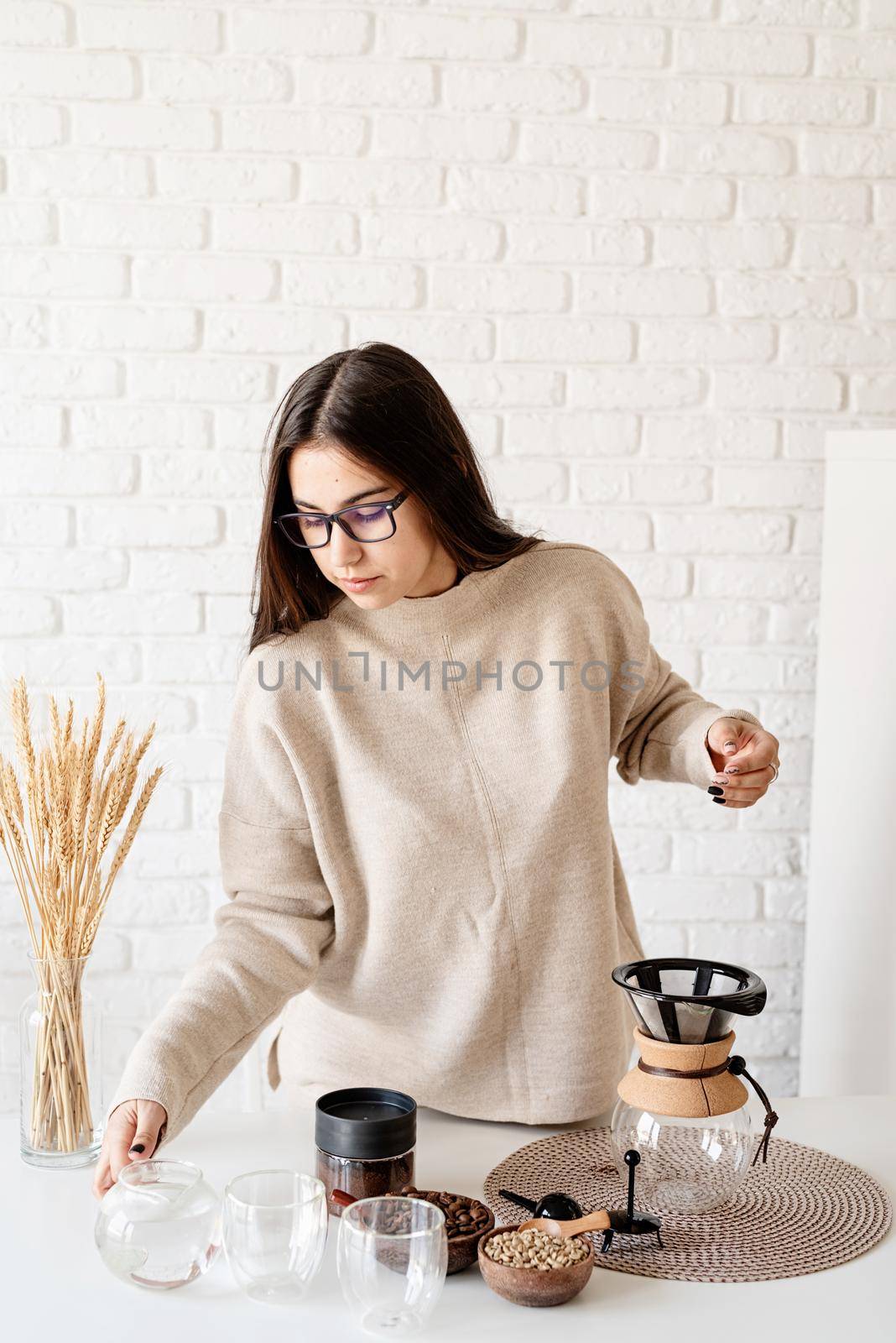 Alternative coffee brewing. Young woman brewing coffee in chemex sitting at the white table with various stuff for alternative coffee brewing
