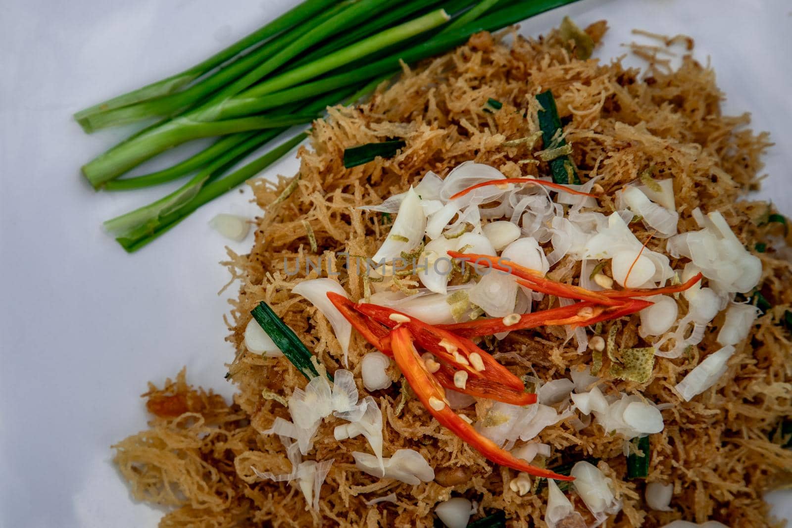 Asian eating food, Mee Grob is an sweet and sour crispy noodles, made from Thai rice noodle with sweet and sour sauce on white plate, Sweet & Sour Crispy Rice Noodles, Close up.