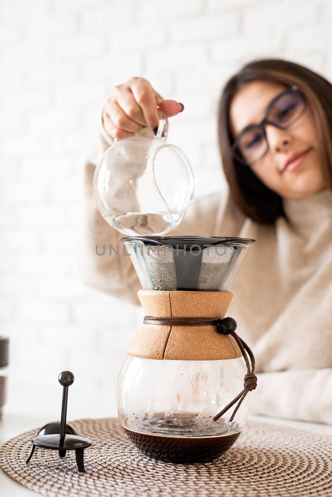 Alternative coffee brewing. Young woman brewing coffee in chemex standing at the white table with various stuff for alternative coffee brewing, pouring hot water into the filter
