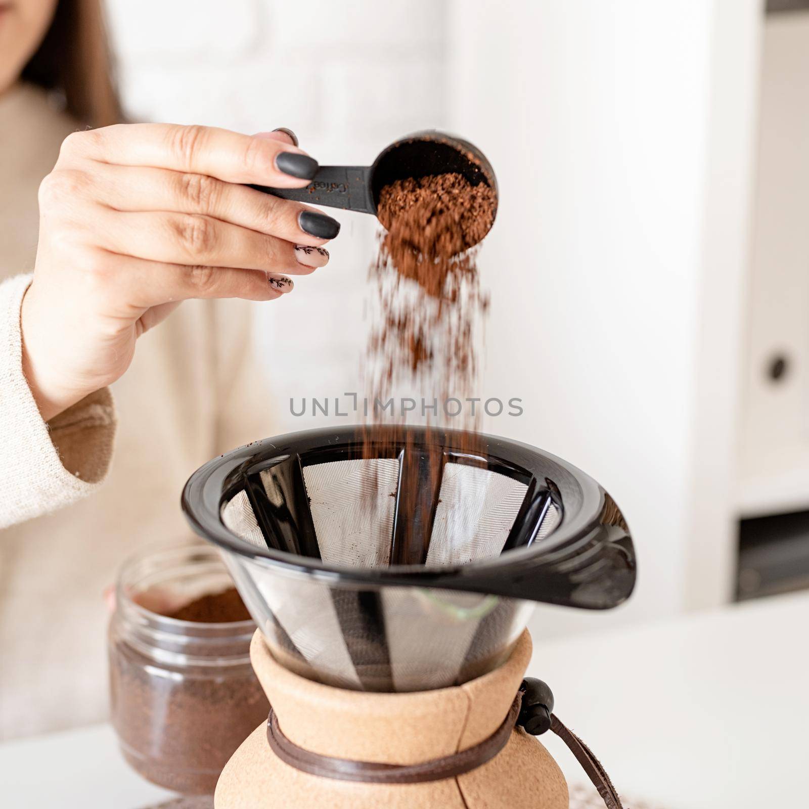 Alternative coffee brewing. Young woman brewing coffee in chemex sitting at the white table with various stuff for alternative coffee brewing, pouring grinded coffee beans into filter