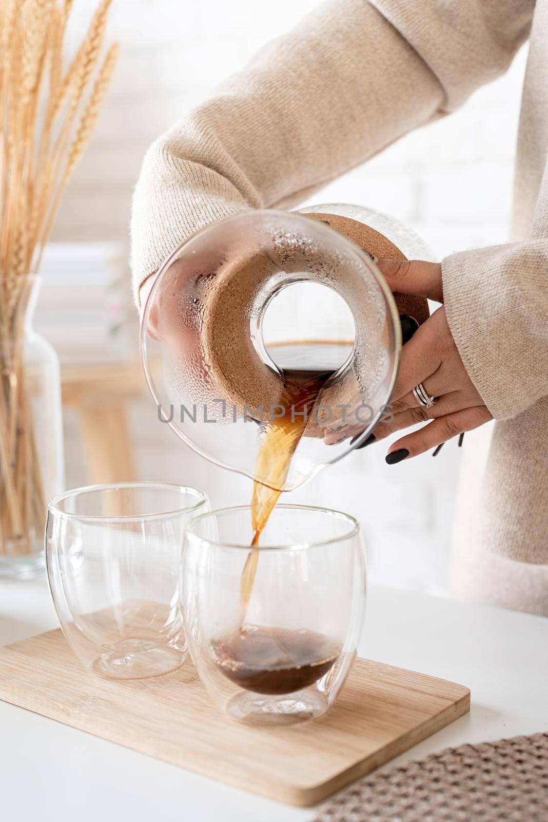 Alternative coffee brewing. Young woman brewing coffee in chemex standing at the white table with various stuff for alternative coffee brewing, pouring coffee to the glass