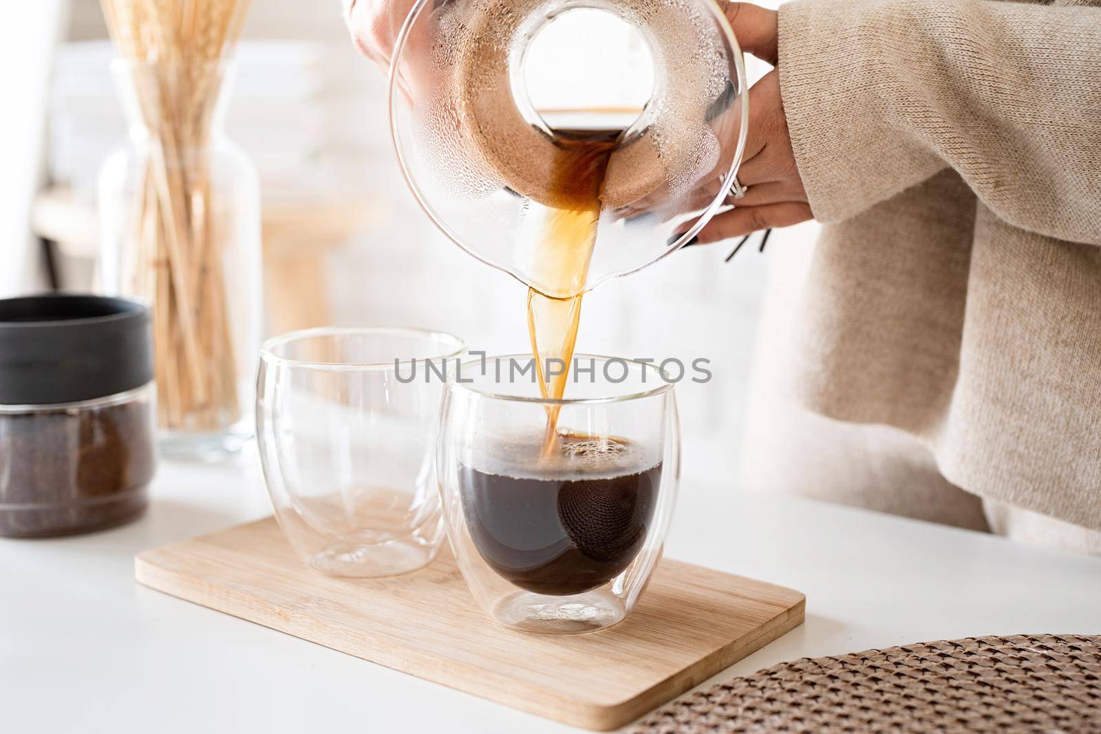 Alternative coffee brewing. Young woman brewing coffee in chemex standing at the white table with various stuff for alternative coffee brewing, pouring coffee to the glass