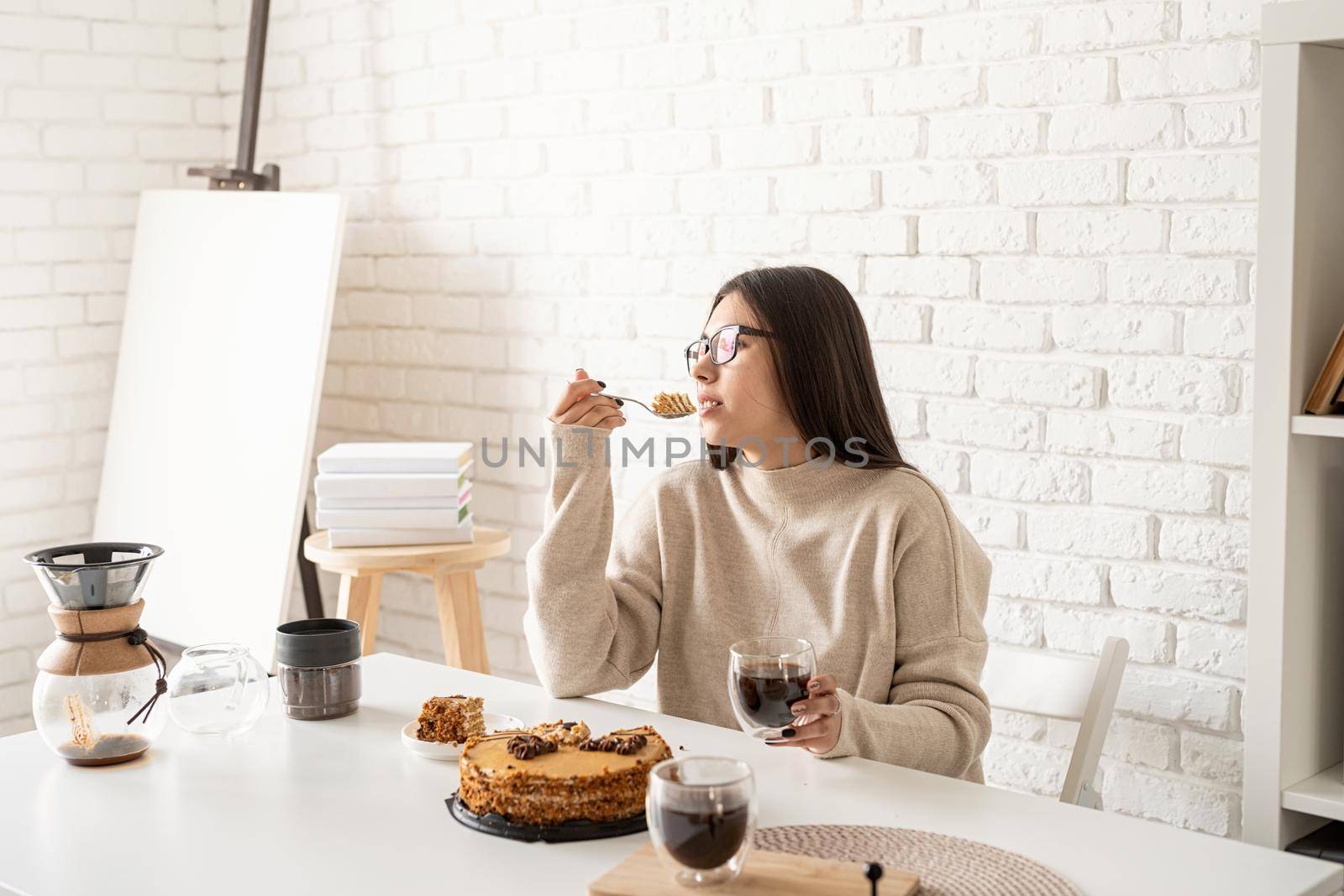 Alternative coffee brewing. Young woman sitting at the white table, eating cake and drinking coffee