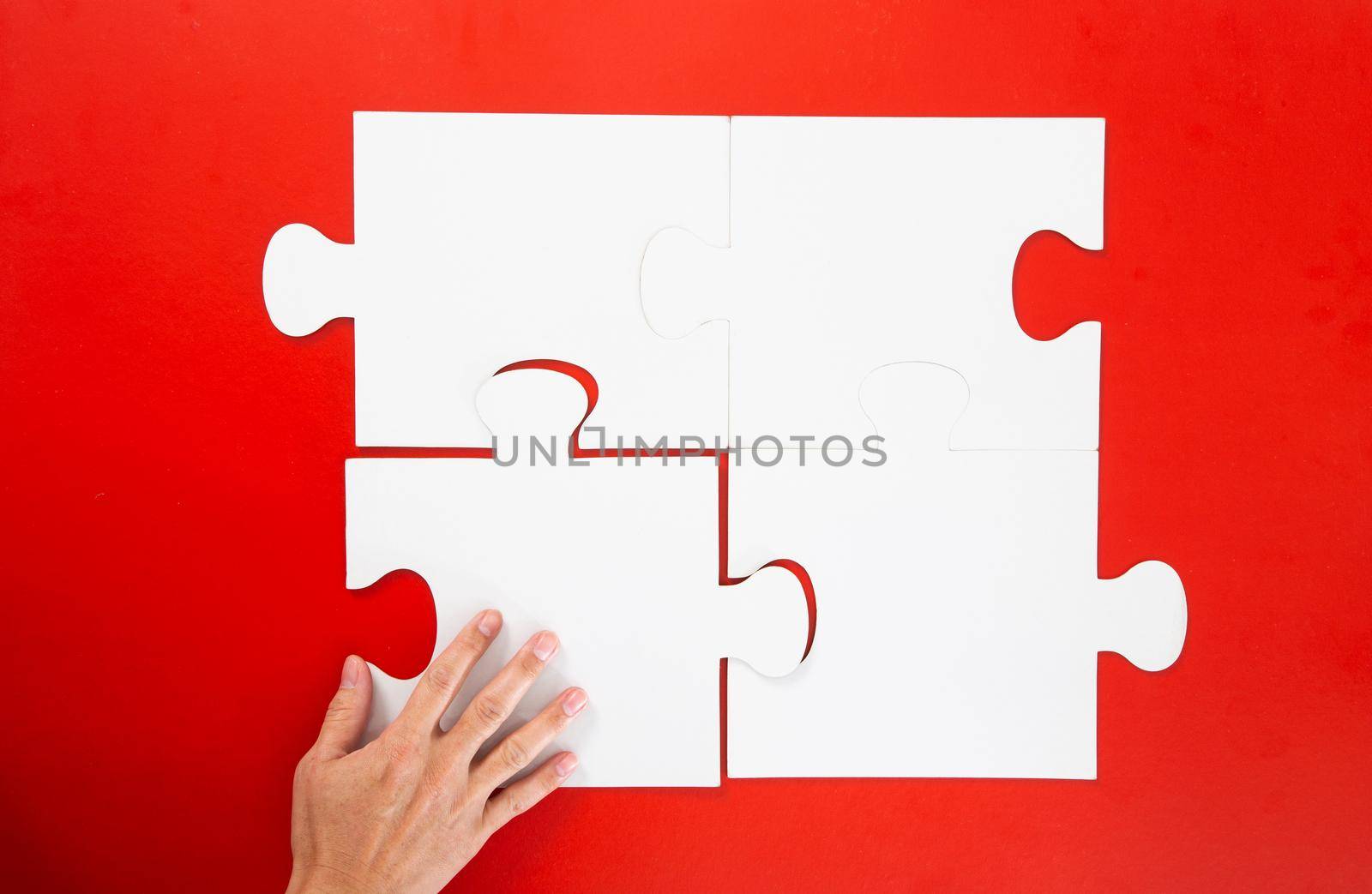hand solving a puzzle piece on red background. by tehcheesiong