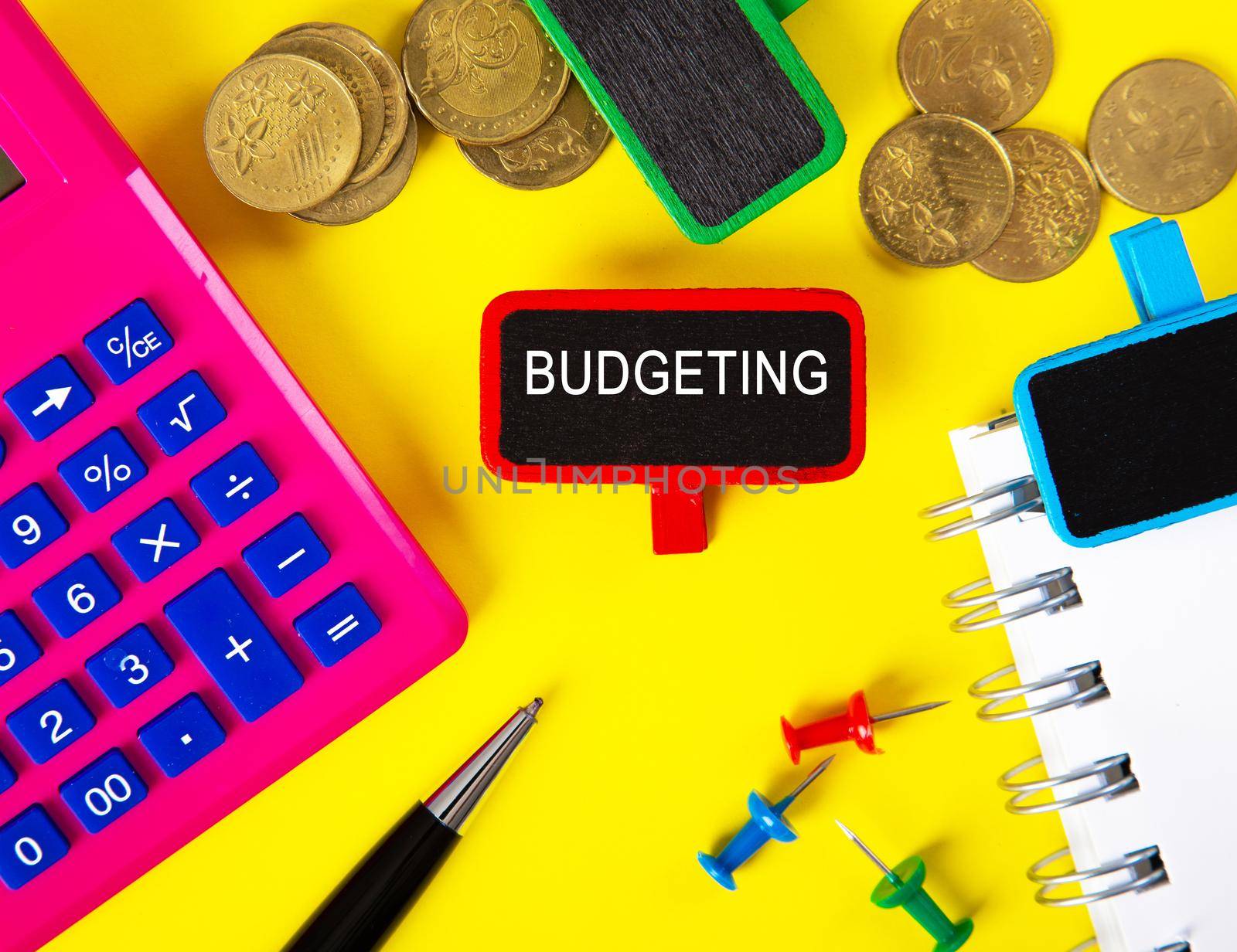 Top view of tag with BUDGETING word with calculator,pen and coins on yellow background table