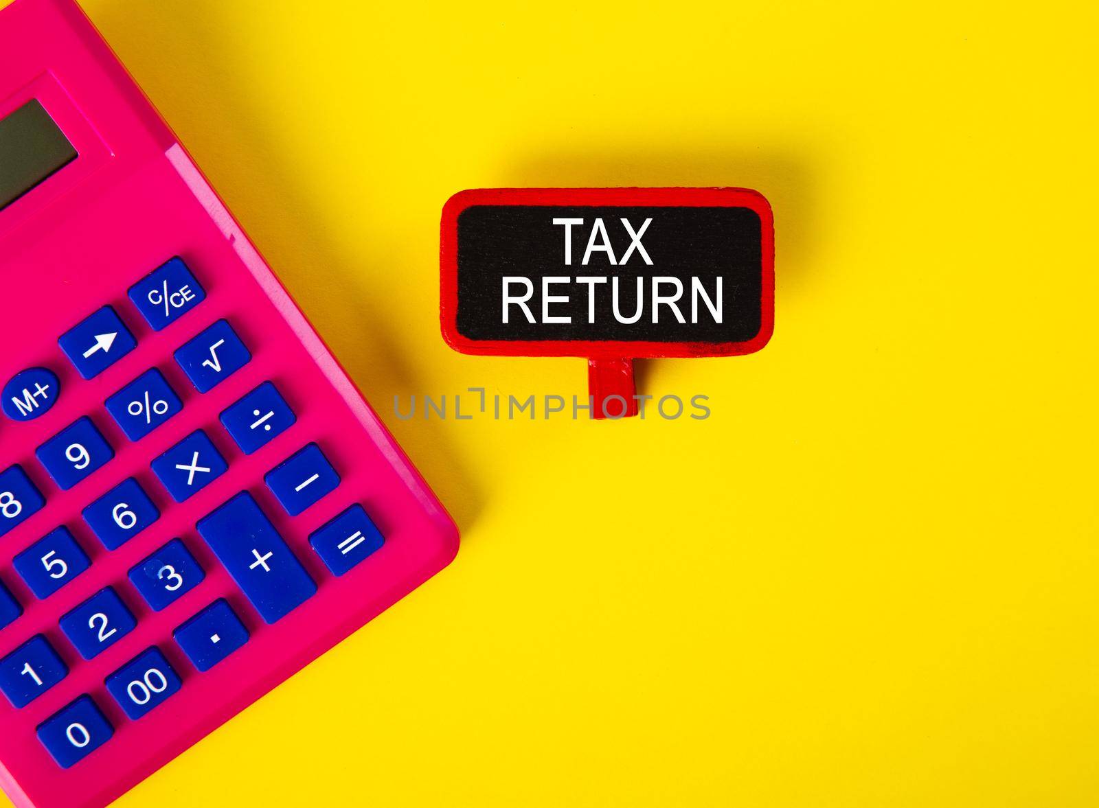 Top view of calculator and a tag with TAX RETURN word on yellow background