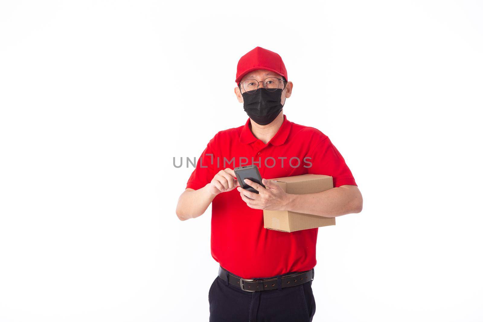 young Asian delivery man in red uniform with  face mask, carrry cardboard box in hands isolated on white background. by tehcheesiong