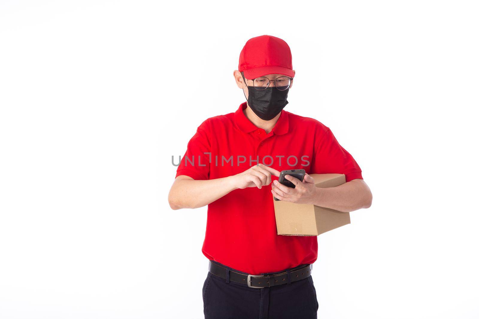 young Asian delivery man in red uniform with  face mask, carrry cardboard box in hands isolated on white background. by tehcheesiong